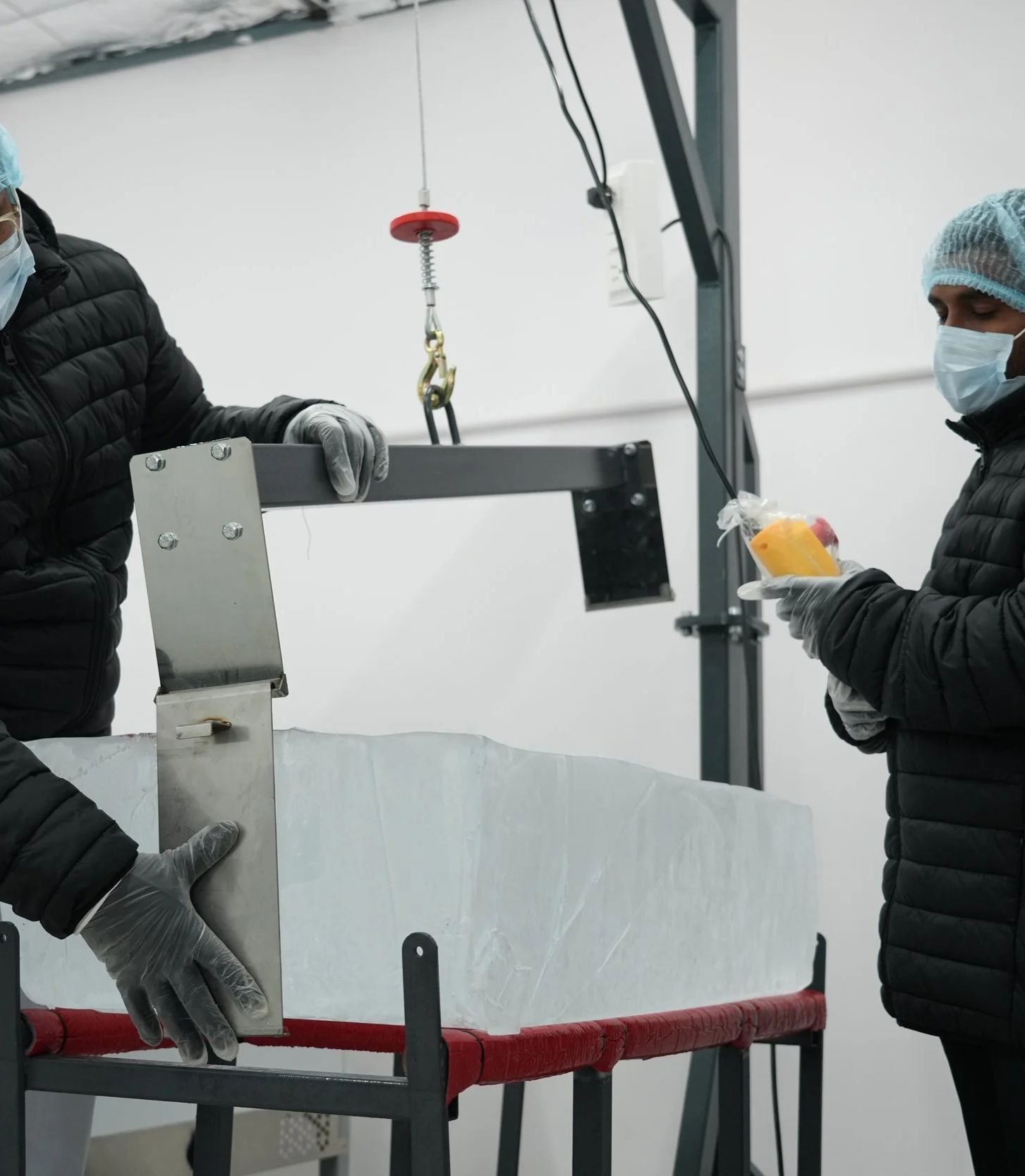 Two people wearing masks and gloves handling a large block of ice in a cold storage room.