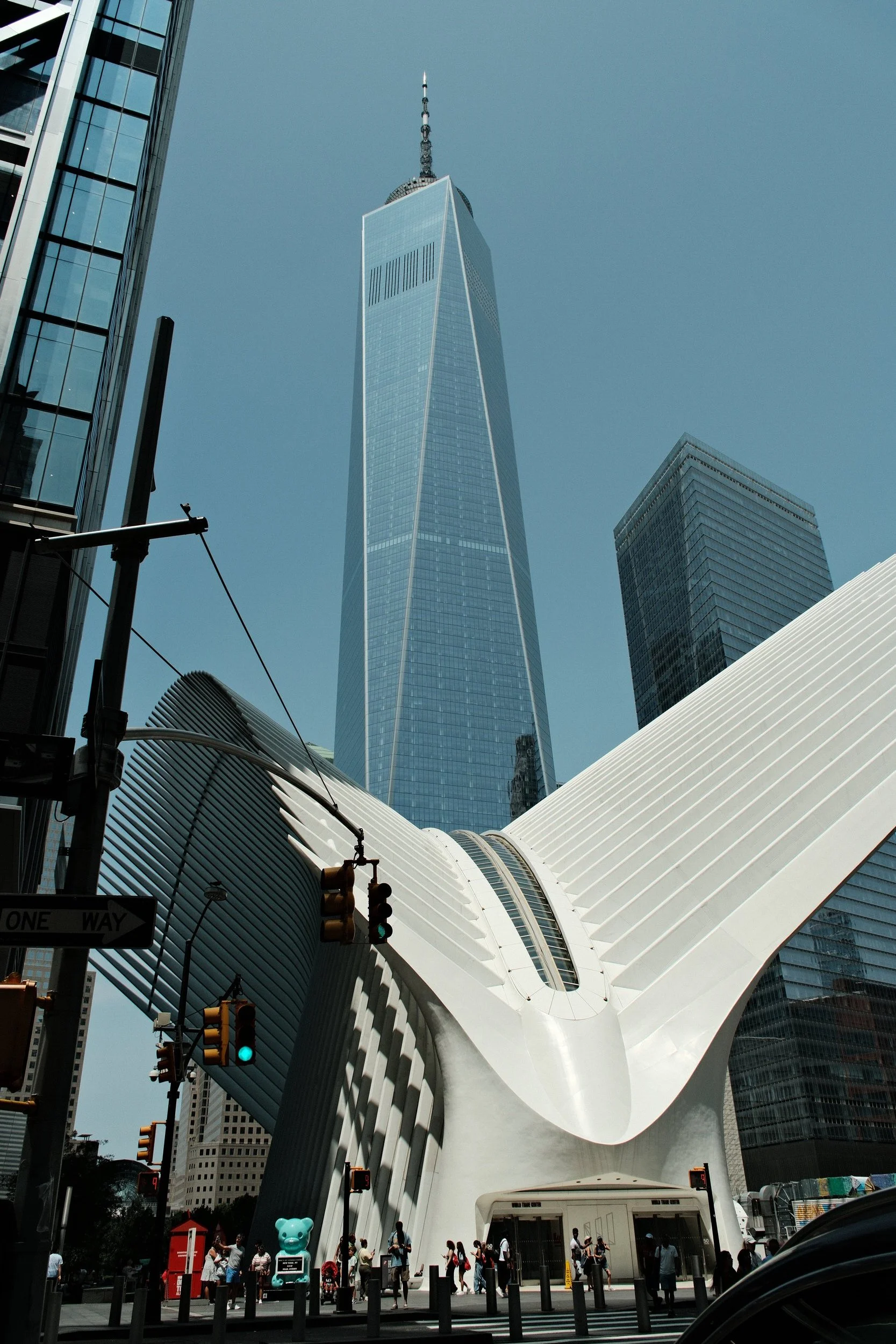 A tall modern skyscraper seen from street level, with a white architectural structure in the foreground, and a group of people walking under it.