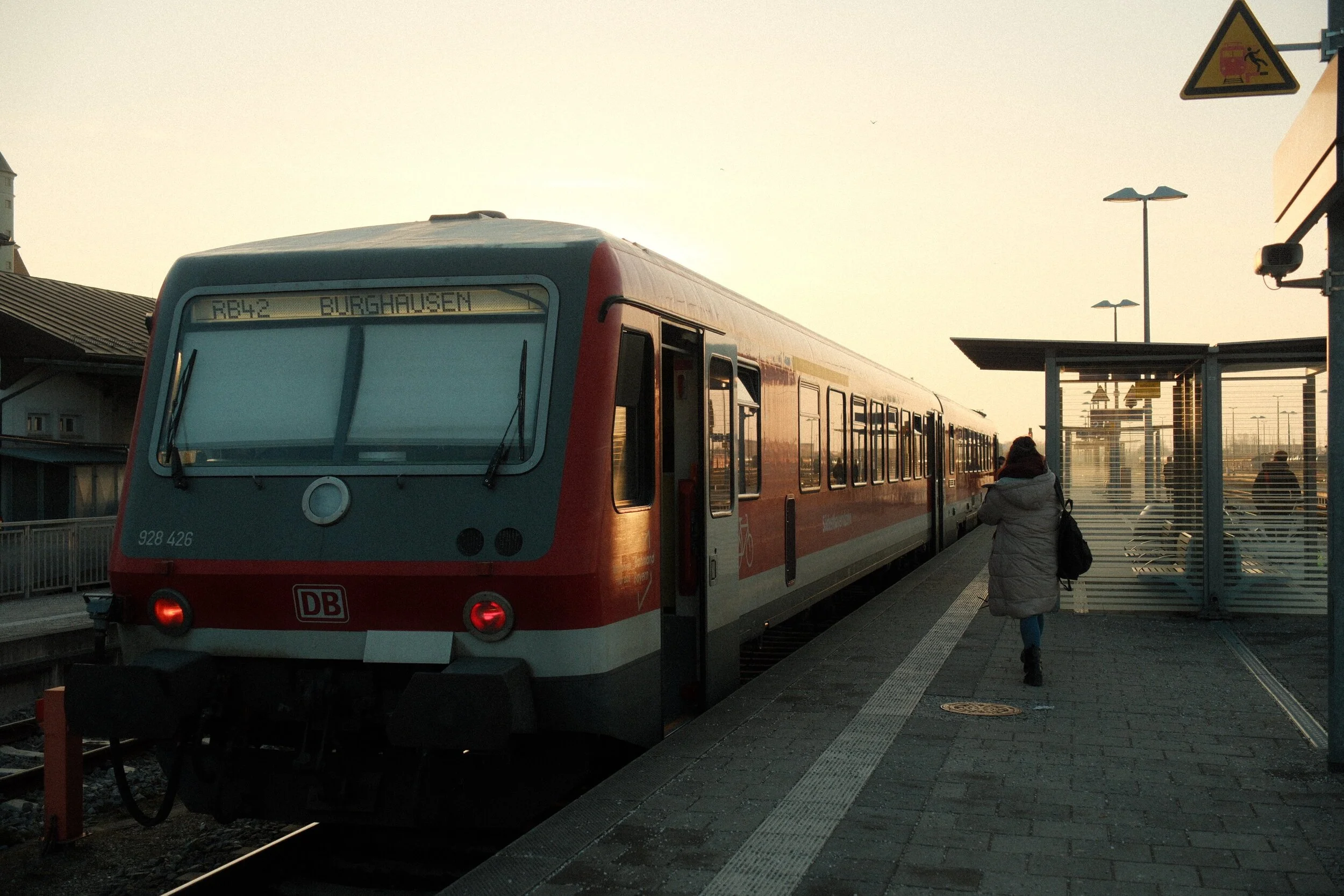 A Deutsche Bahn train at a platform with a person walking towards it, in the early morning or late afternoon light.