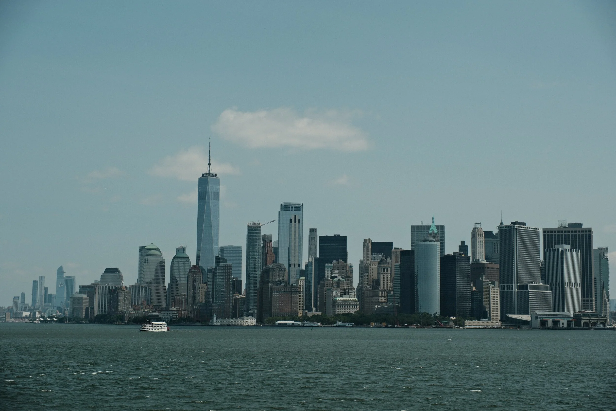 View of New York City skyline with One World Trade Center, skyscrapers, and waterfront with boat in the foreground.