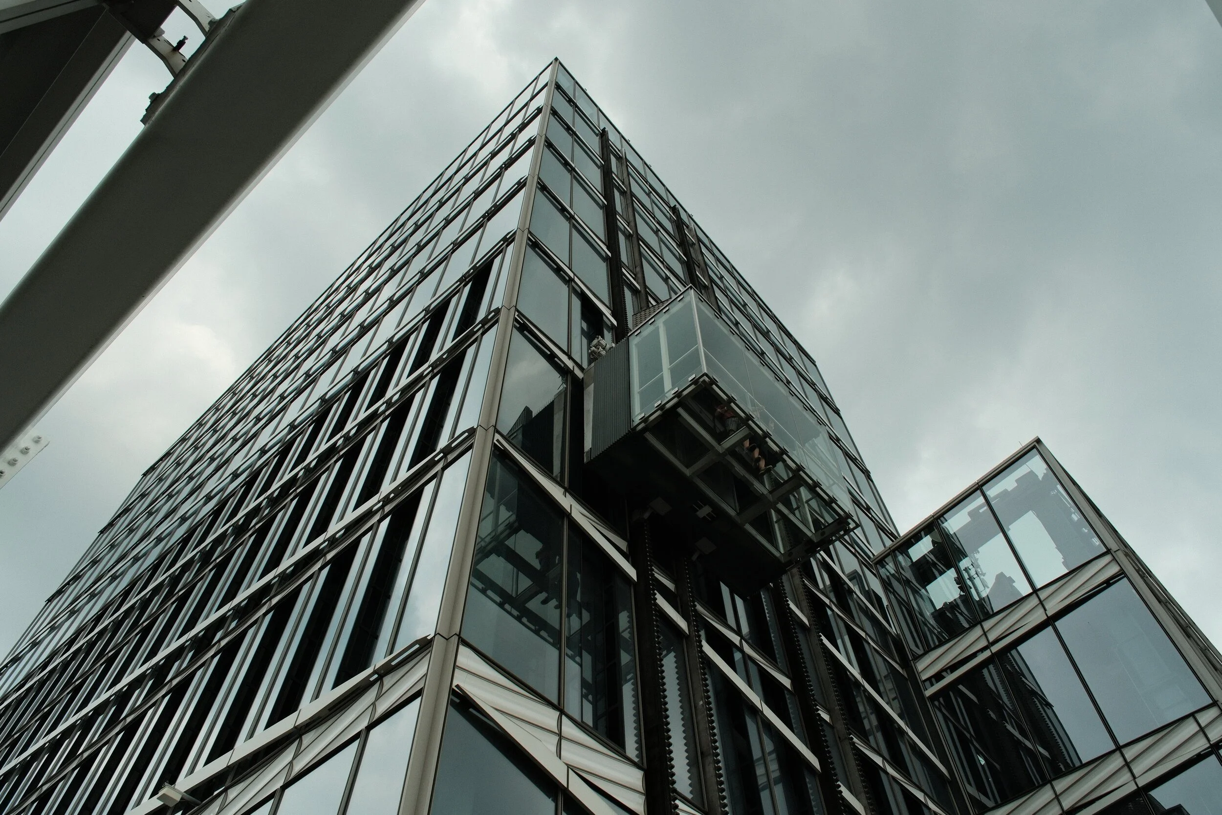 Upside-down view of a modern glass office building against a cloudy sky.