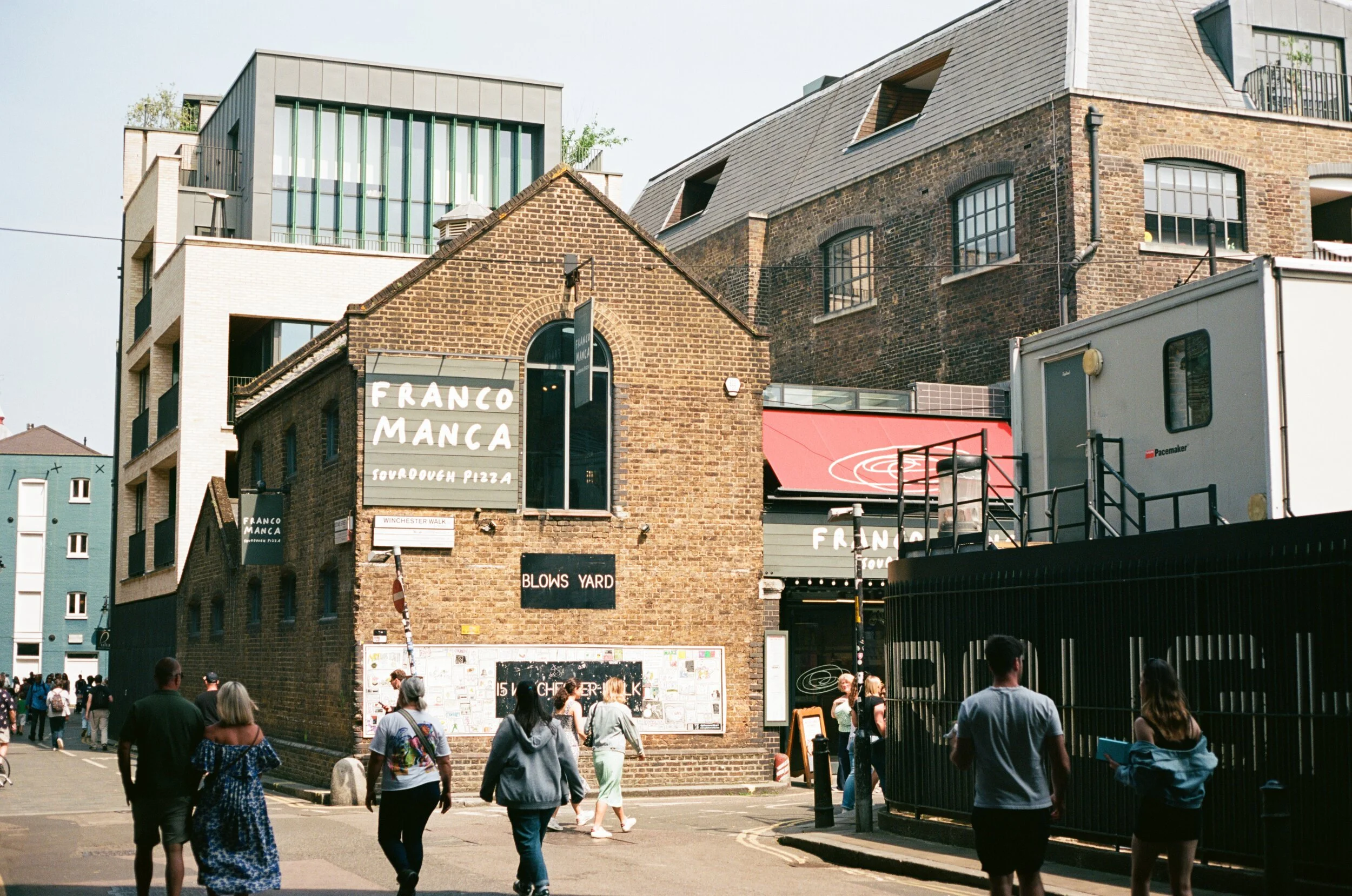 Street view of The Franco Manca restaurant on Winchester Walk, with people walking past on the sidewalk, surrounded by modern and historic buildings.