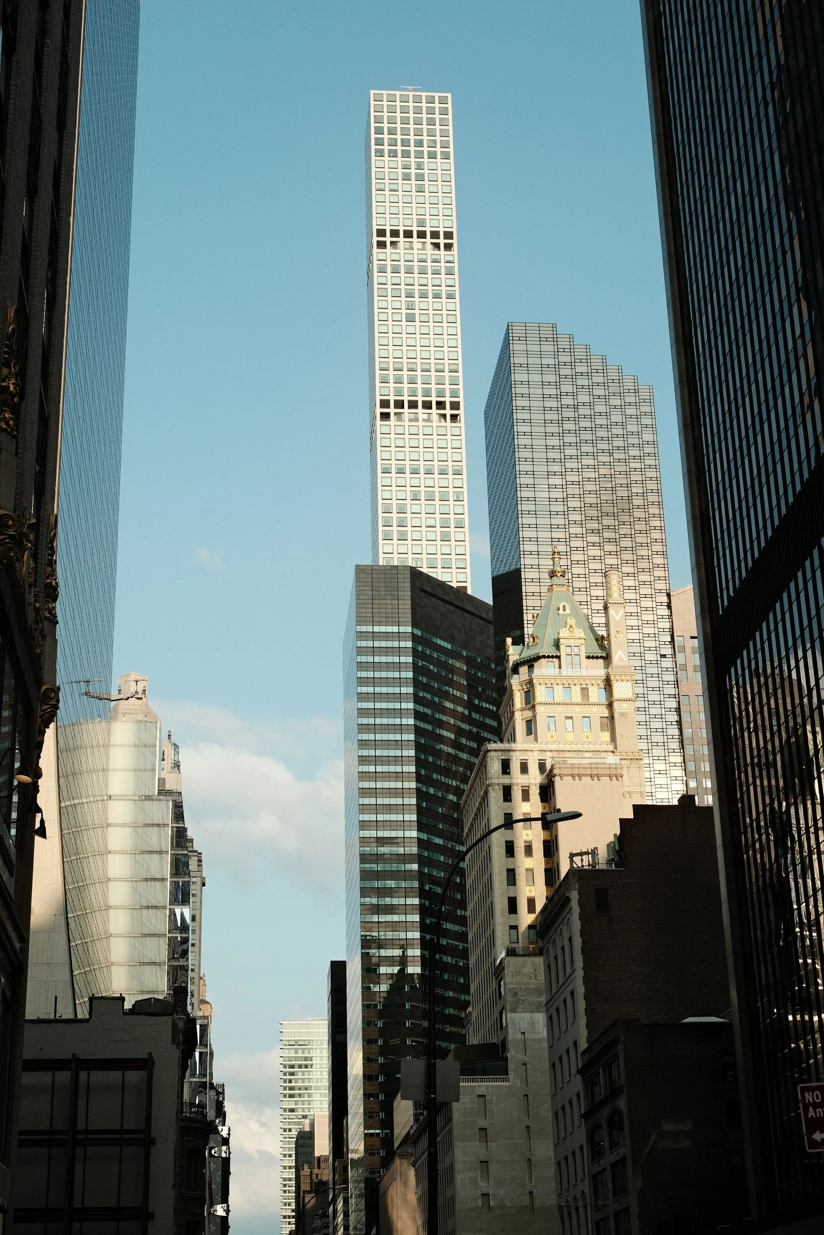 Tall skyscrapers in a city with a clear blue sky, viewed from a narrow street between buildings.