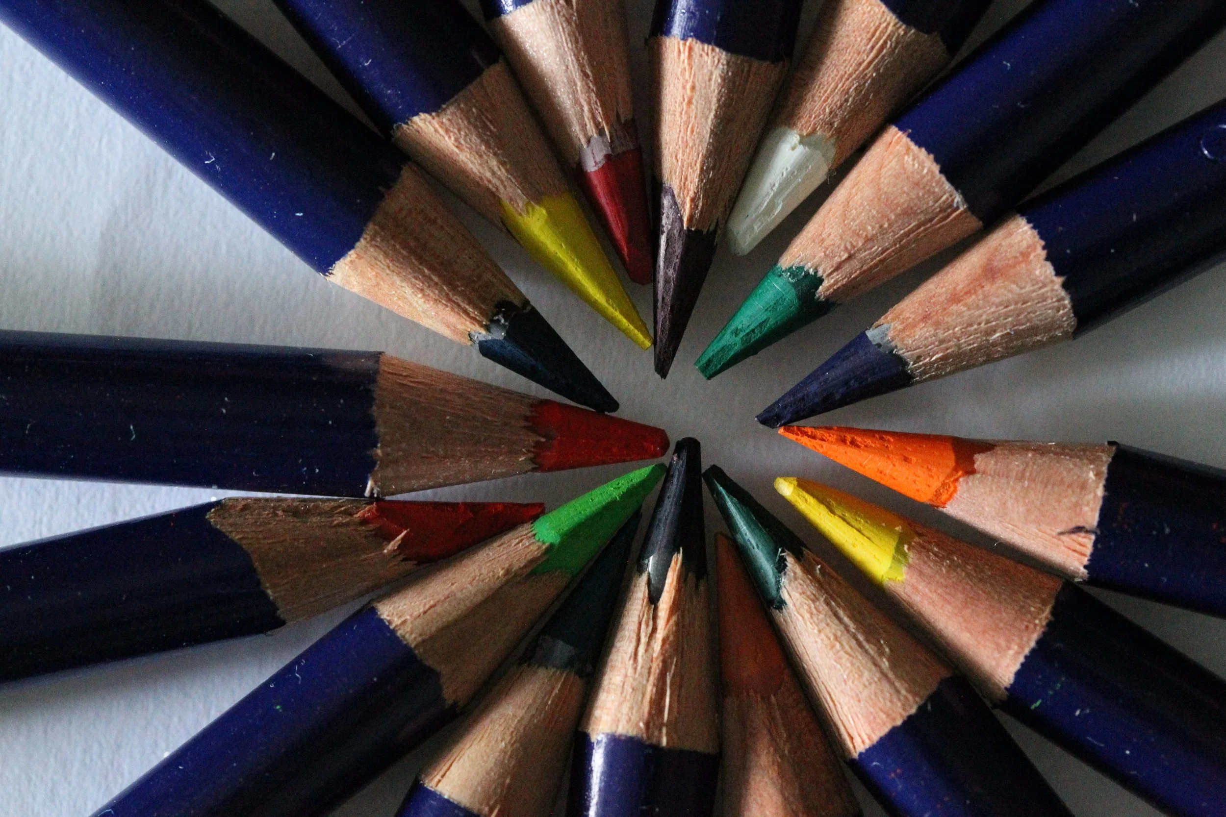 A top-down view of colored pencils arranged in a circle, with sharpened tips pointing towards the center.