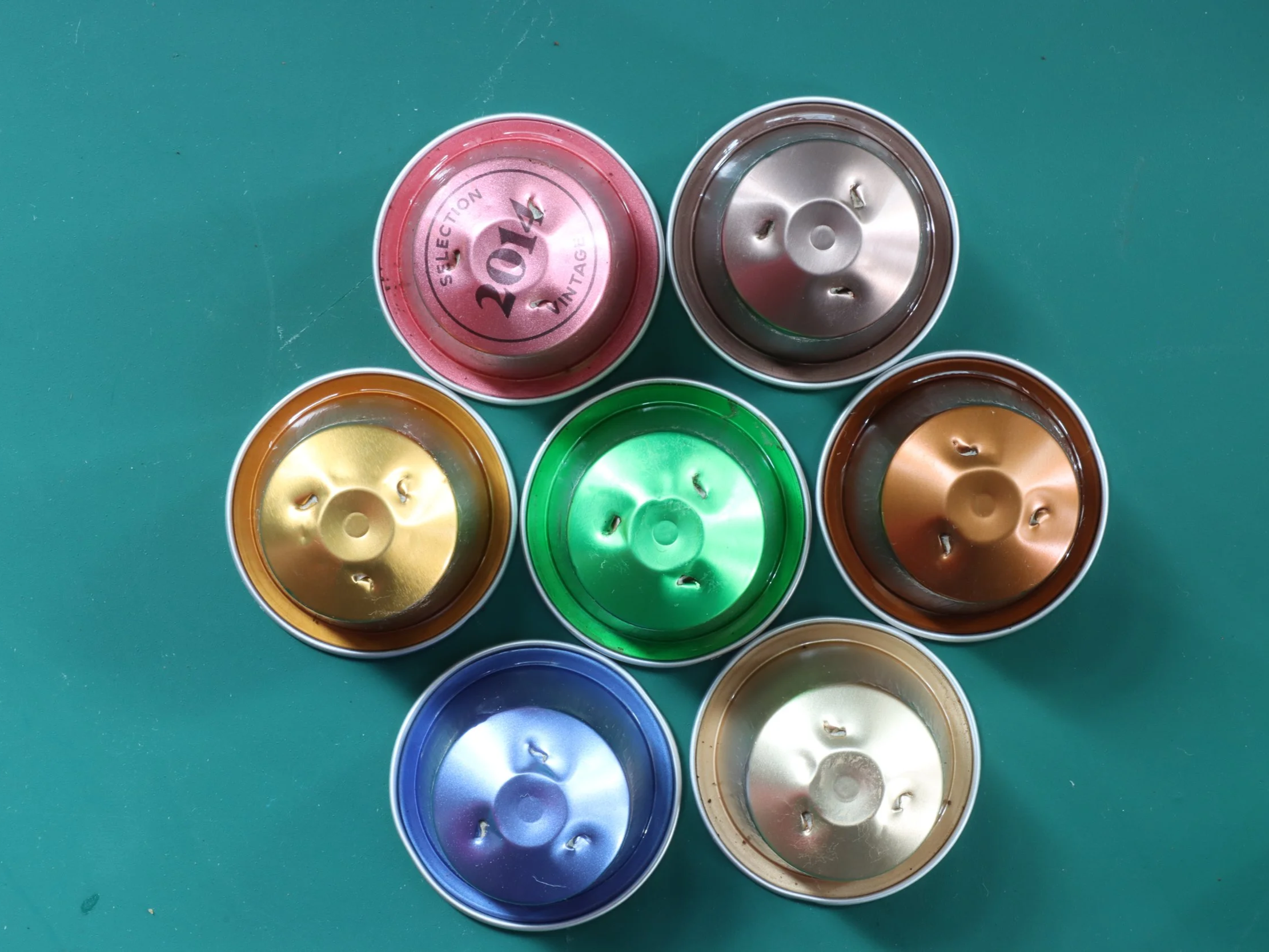 Colourful coffee capsules arranged in a circular pattern on a teal surface.