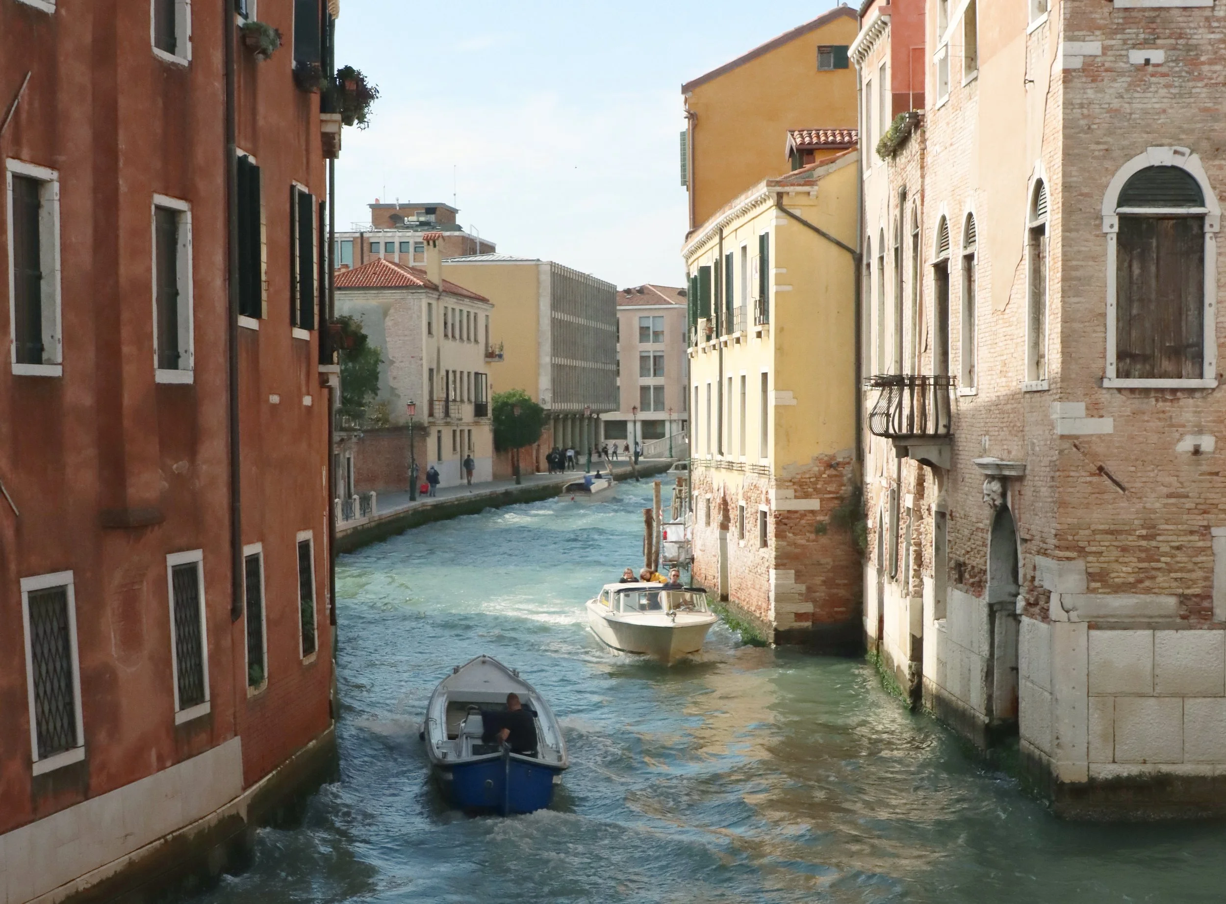 Boats traveling through a narrow canal with colorful buildings on either side in Venice, Italy.