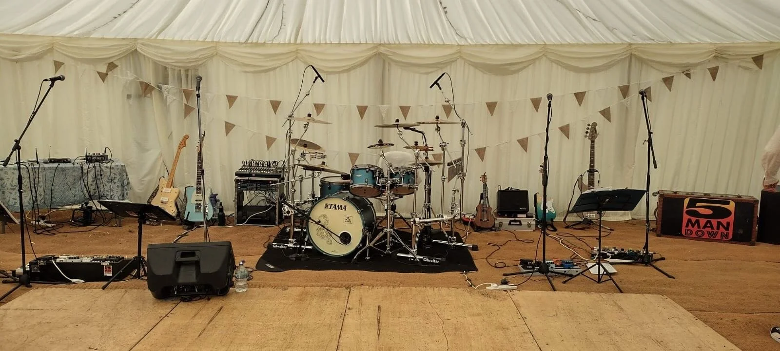 Empty stage setup with drums, guitars, microphones, and sound equipment in a decorated tent.