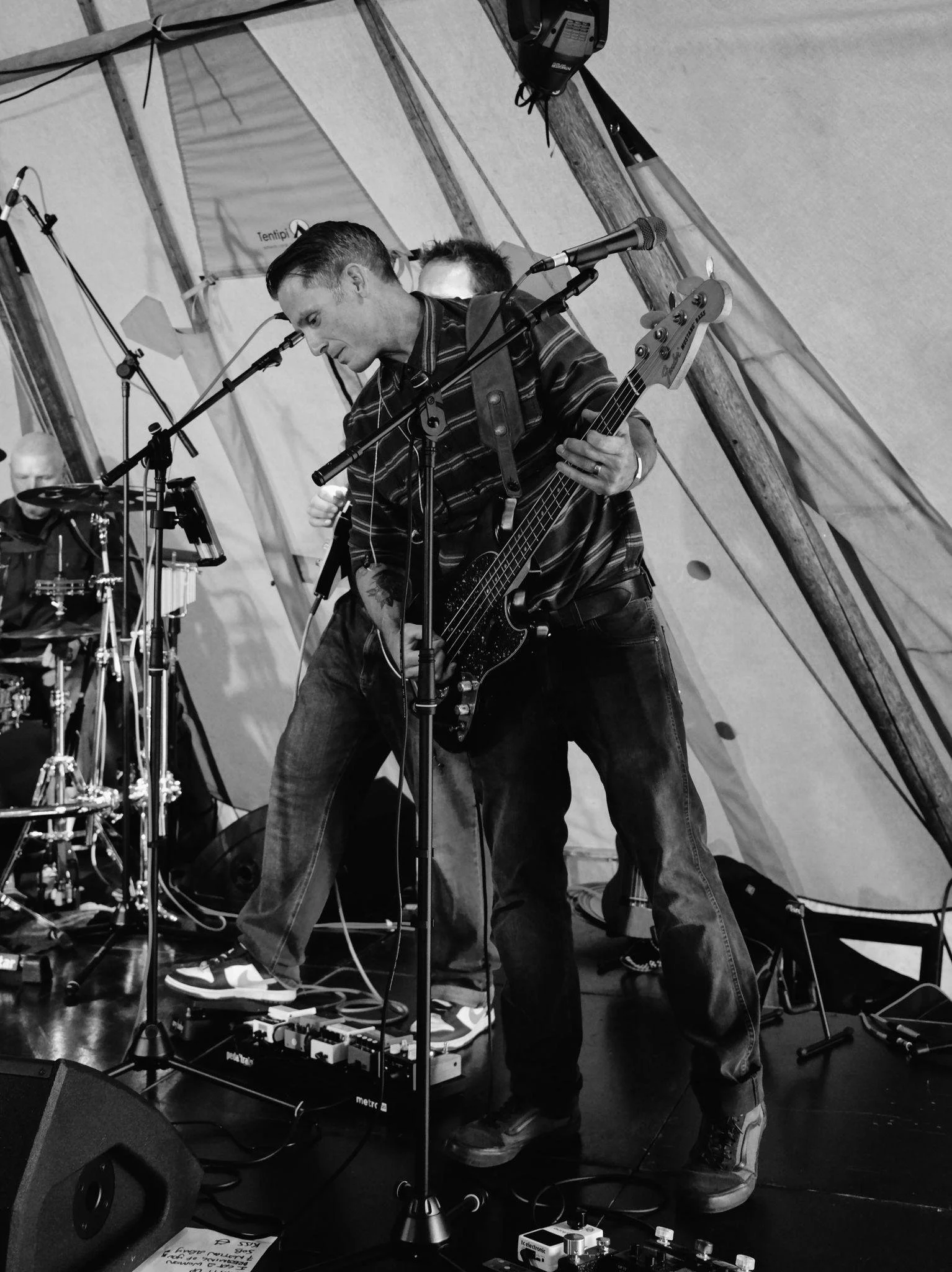 Tom Barnett from 5 Man Down playing electric bass and singing into a microphone during a live performance under a tent.