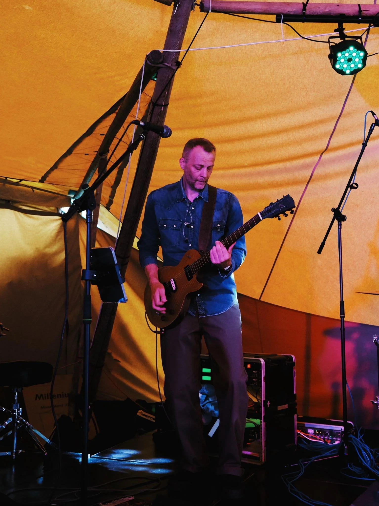 Matt Argyle from 5 Man Down in a denim shirt playing an electric guitar on stage under a yellow tent.