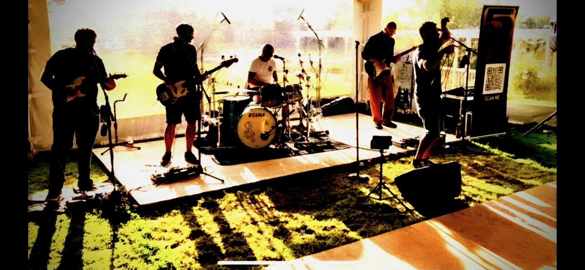5 Man Down musicians performing on a stage outdoors, with a bright and vibrant backdrop and natural lighting.