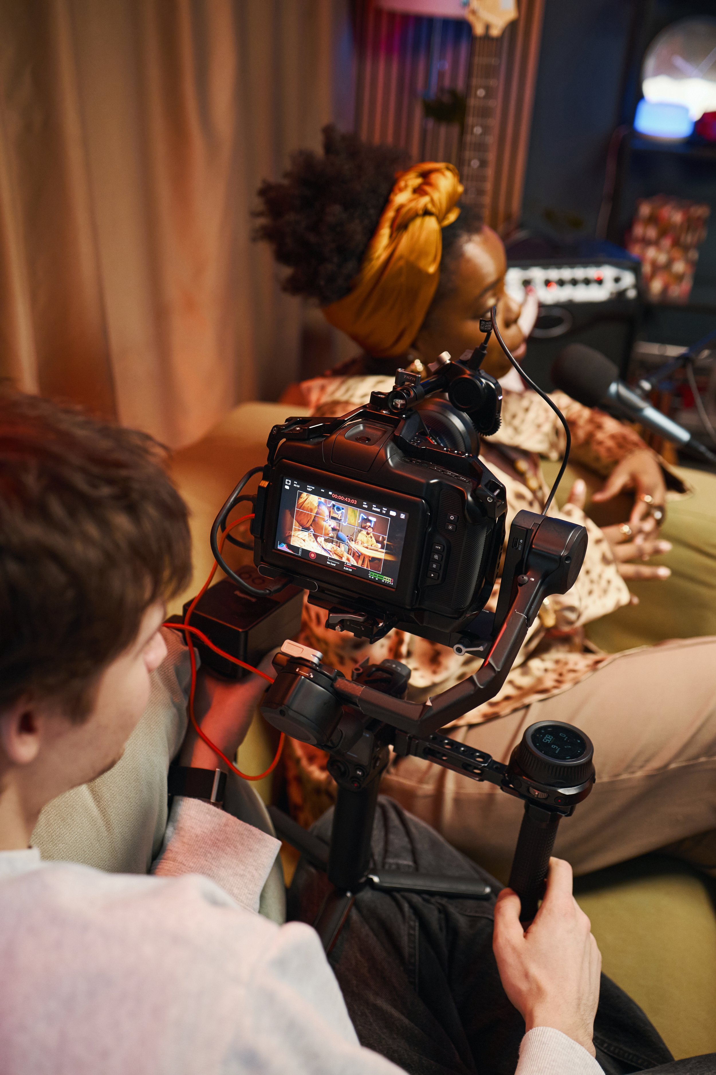 Filmmaker filming woman speaking into microphone, with camera and recording equipment in a recording studio.