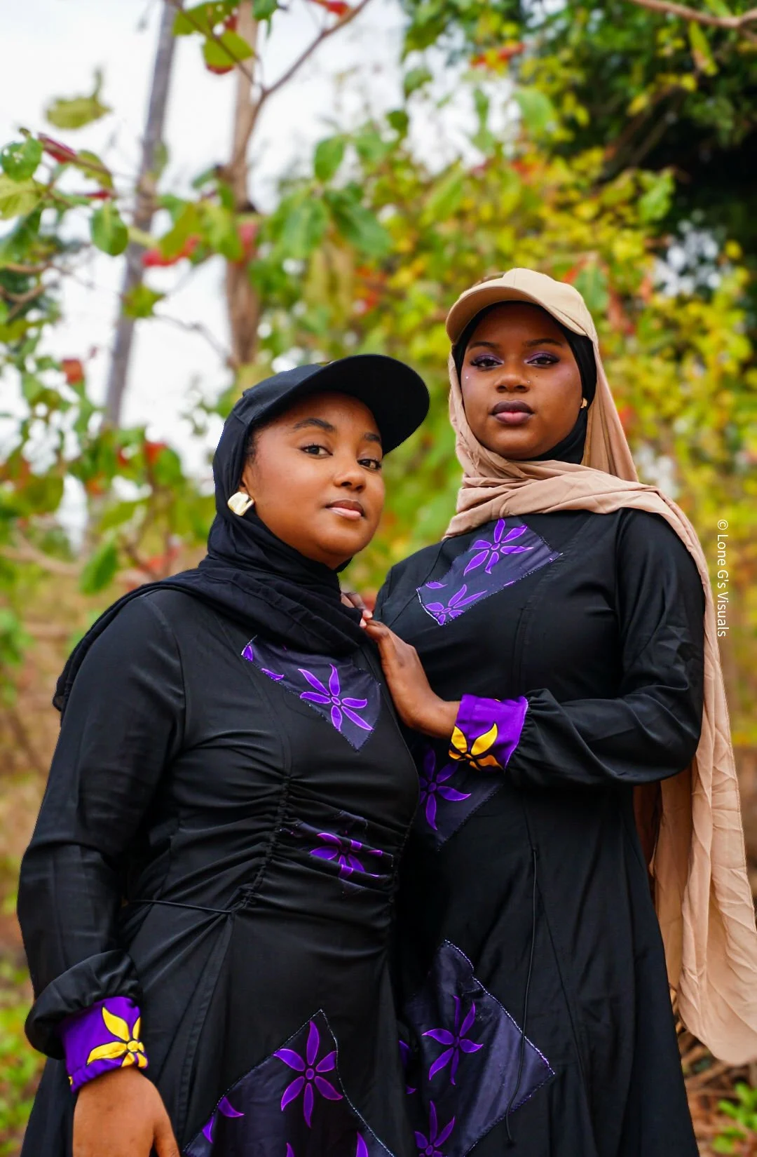 Deux femmes portant un burkini noir avec des motifs ylang violets, debout dans un environnement naturel avec des arbres en arrière-plan.