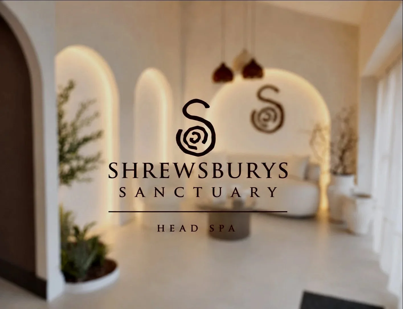 Interior of a spa with high arched windows, white walls, and elegant decor, featuring the logo and name of Shrewsbury Sanctuary Head Spa prominently displayed.
