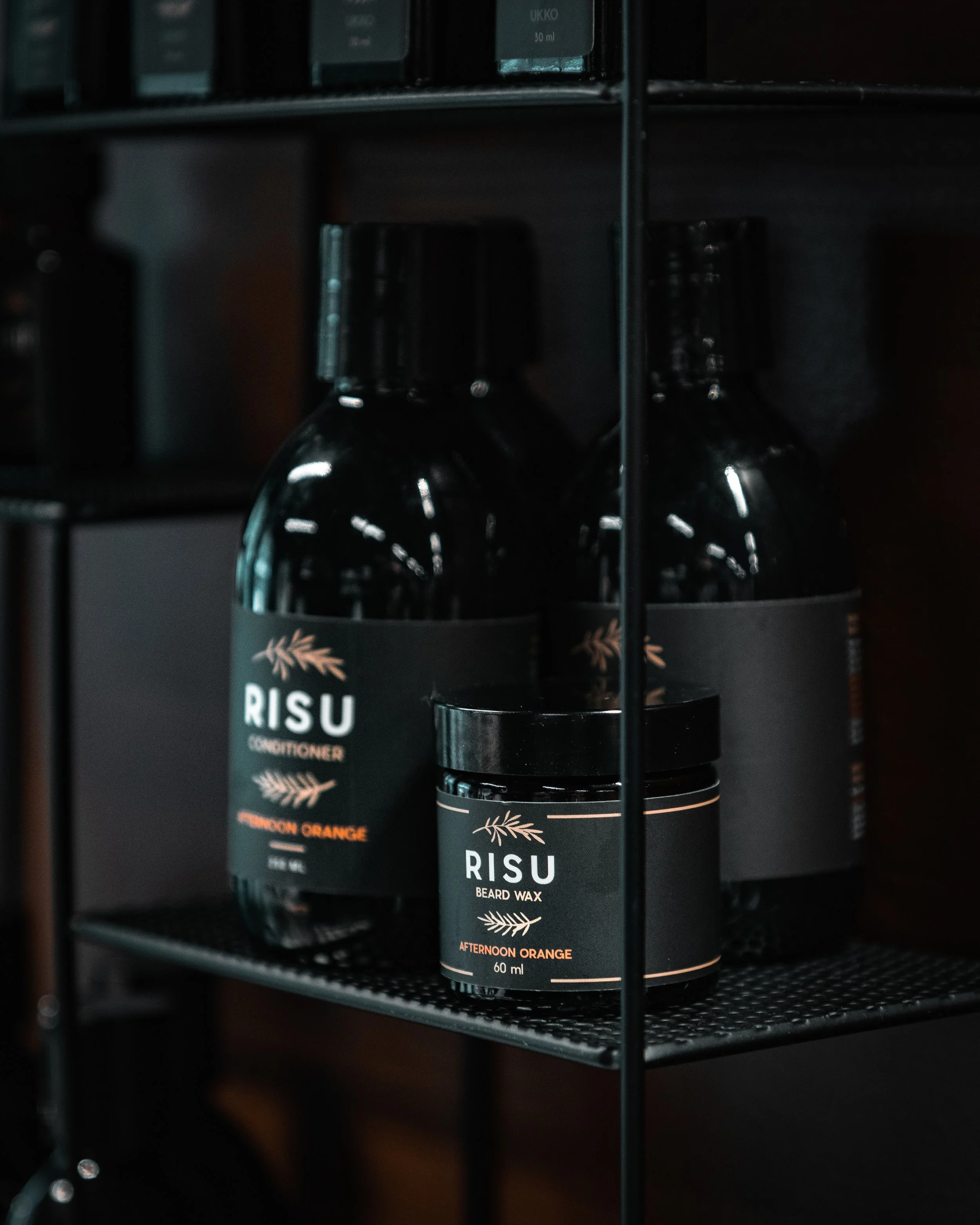 Two black containers labeled 'RISU' with orange accents, one is a conditioner and the other is beard wax, on a black metal shelf.