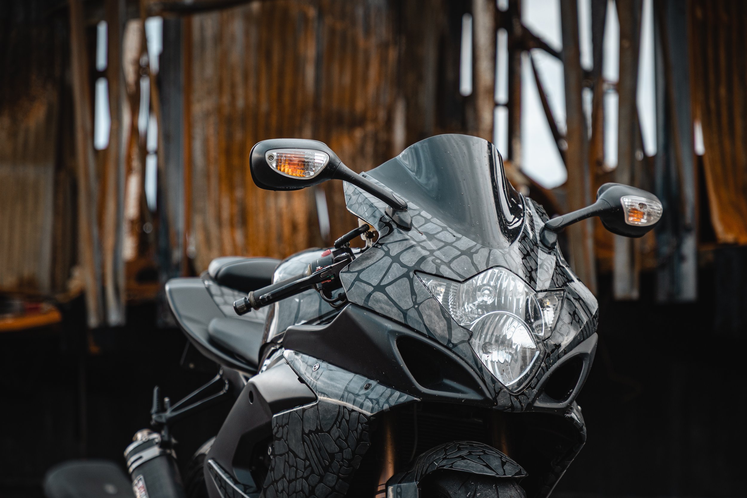 Close-up of a black motorcycle with a textured, cracked pattern on its body, parked inside a rustic wooden barn.