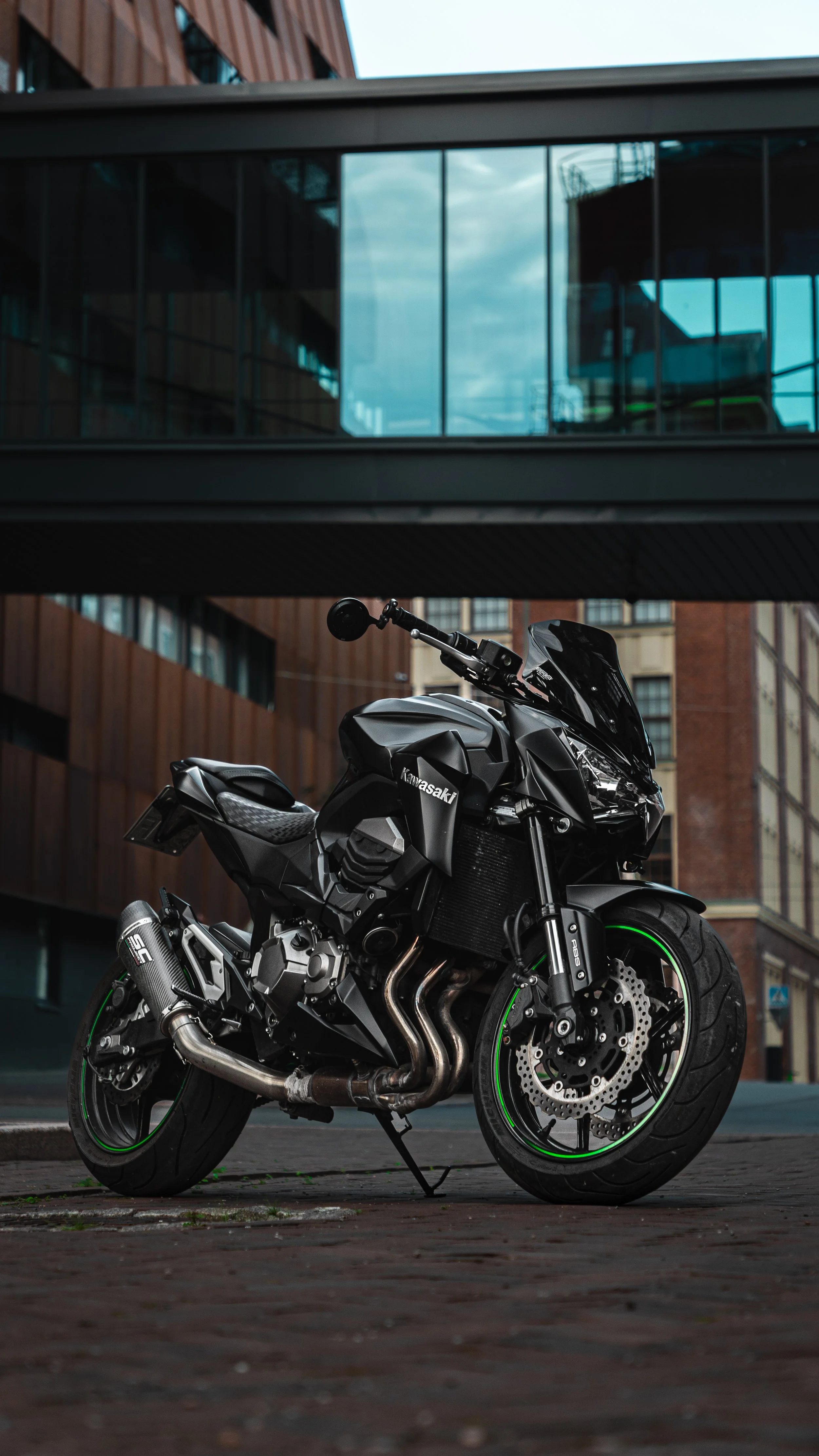 A black Kawasaki sport motorcycle parked on a city street in front of modern buildings with large glass windows.