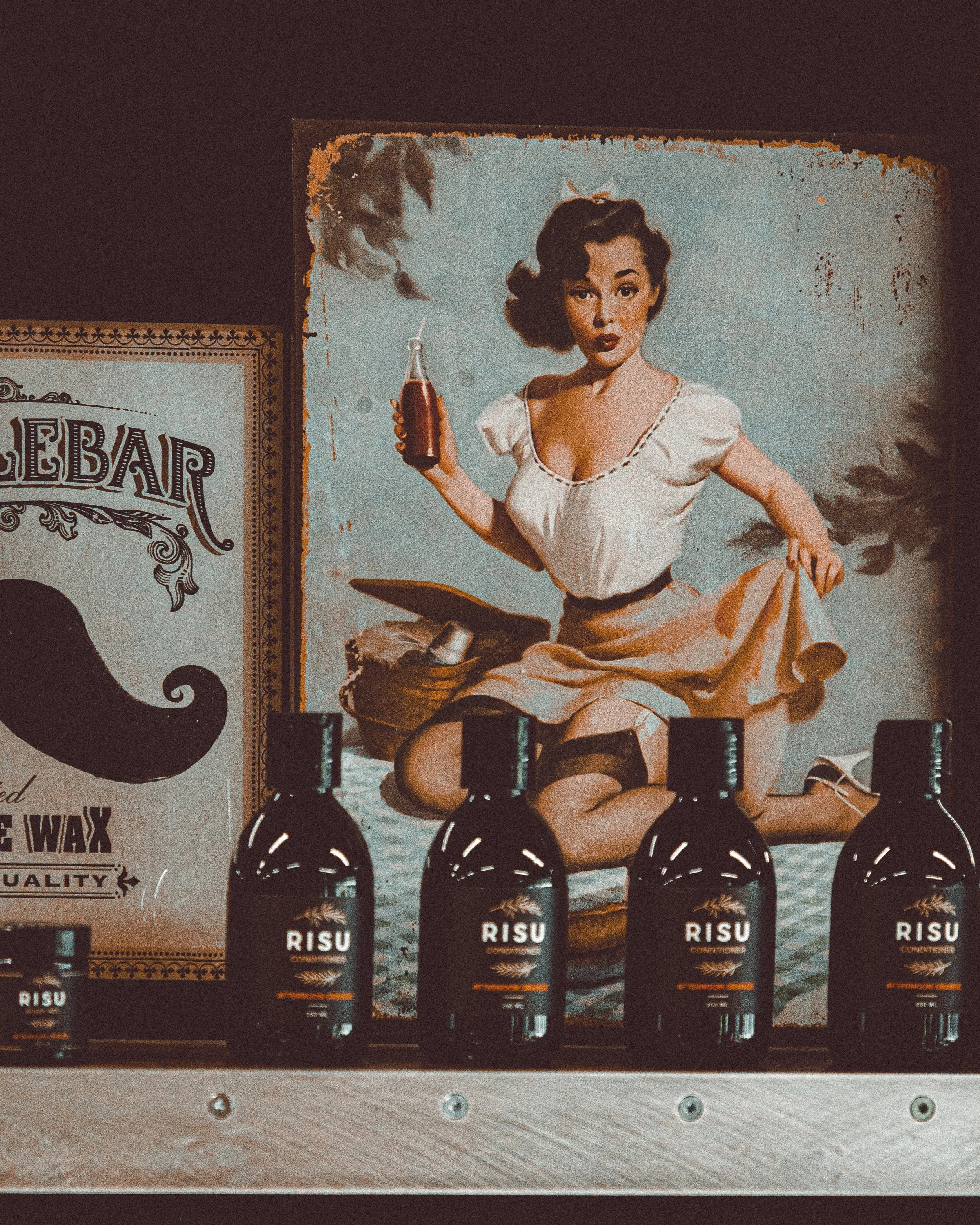 Vintage-style poster of a woman with dark hair holding a soda bottle, sitting with one knee up, surrounded by bottles of RISU conditioner on a wooden surface.