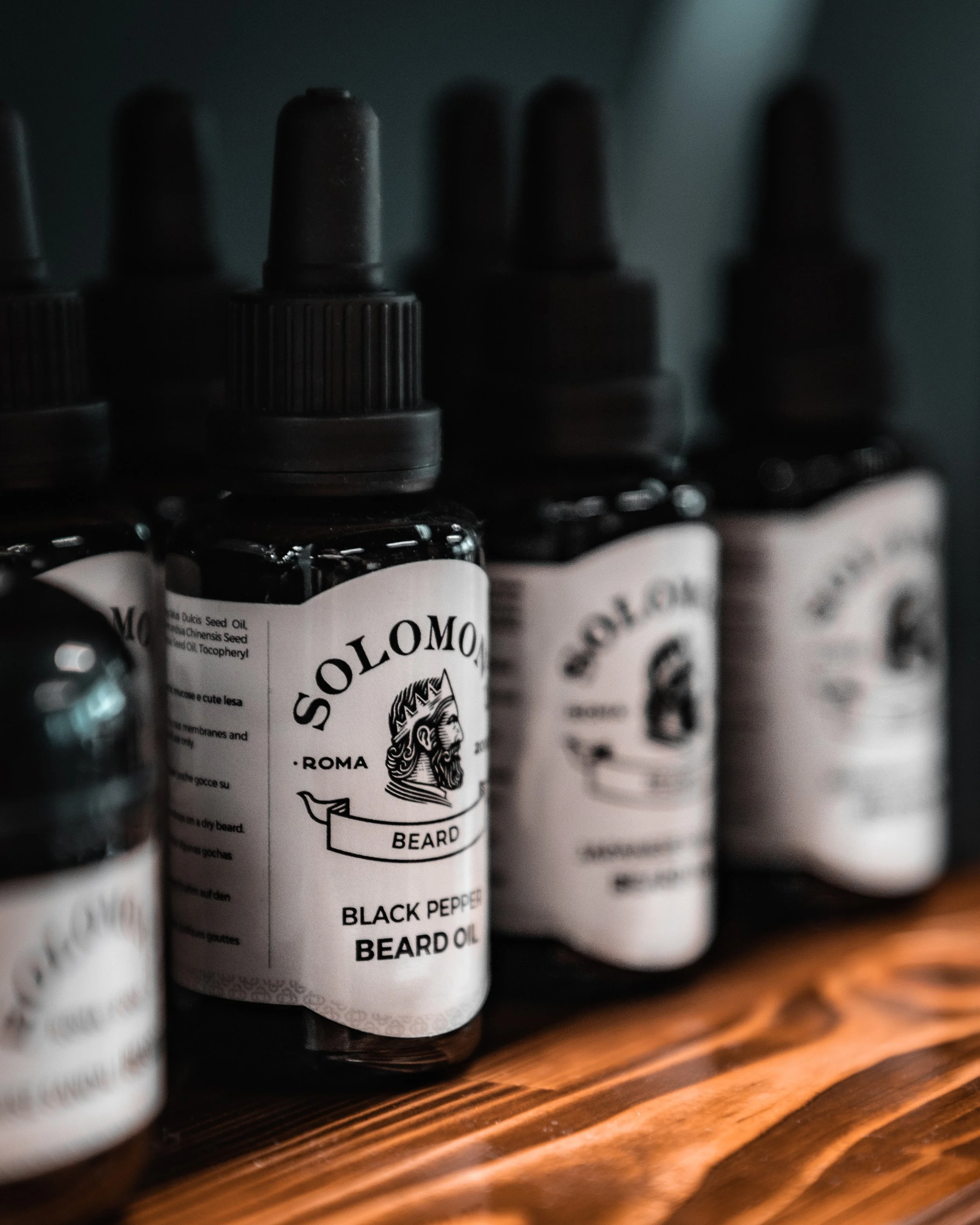 Row of Solomon Roma beard oil bottles with black caps on a wooden surface.