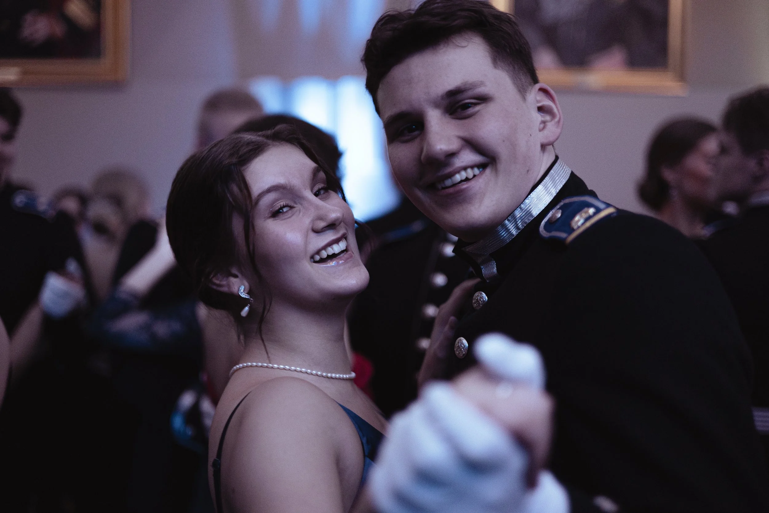 A young woman and a young man in military uniform dancing and smiling at a formal event or ball.
