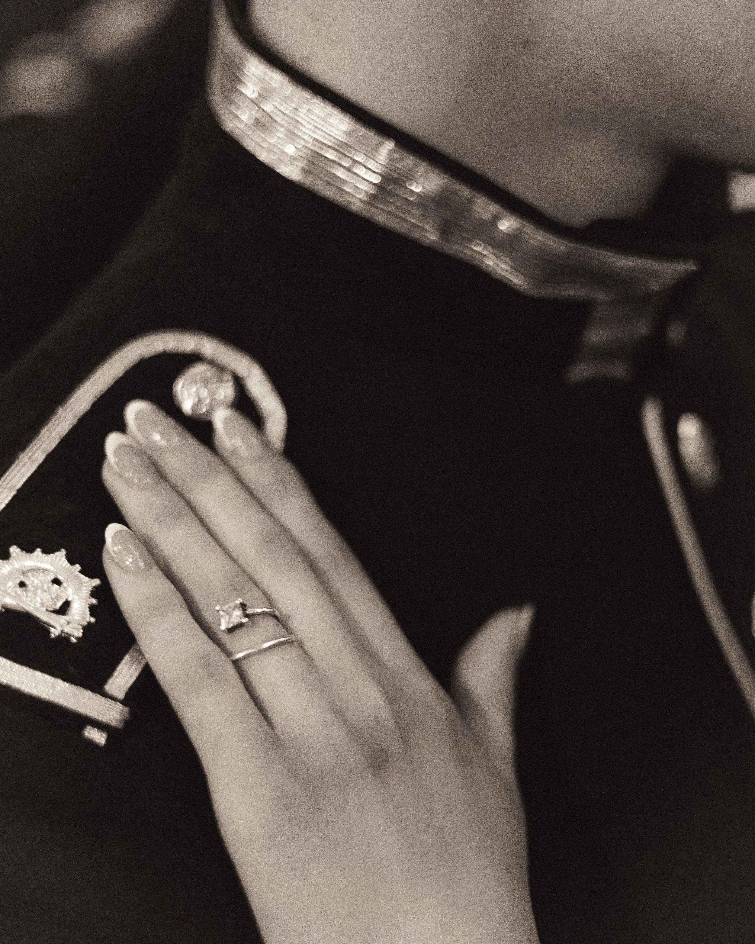 A hand with rings resting on a box of jewelry, including earrings and a necklace, in a dimly lit setting.
