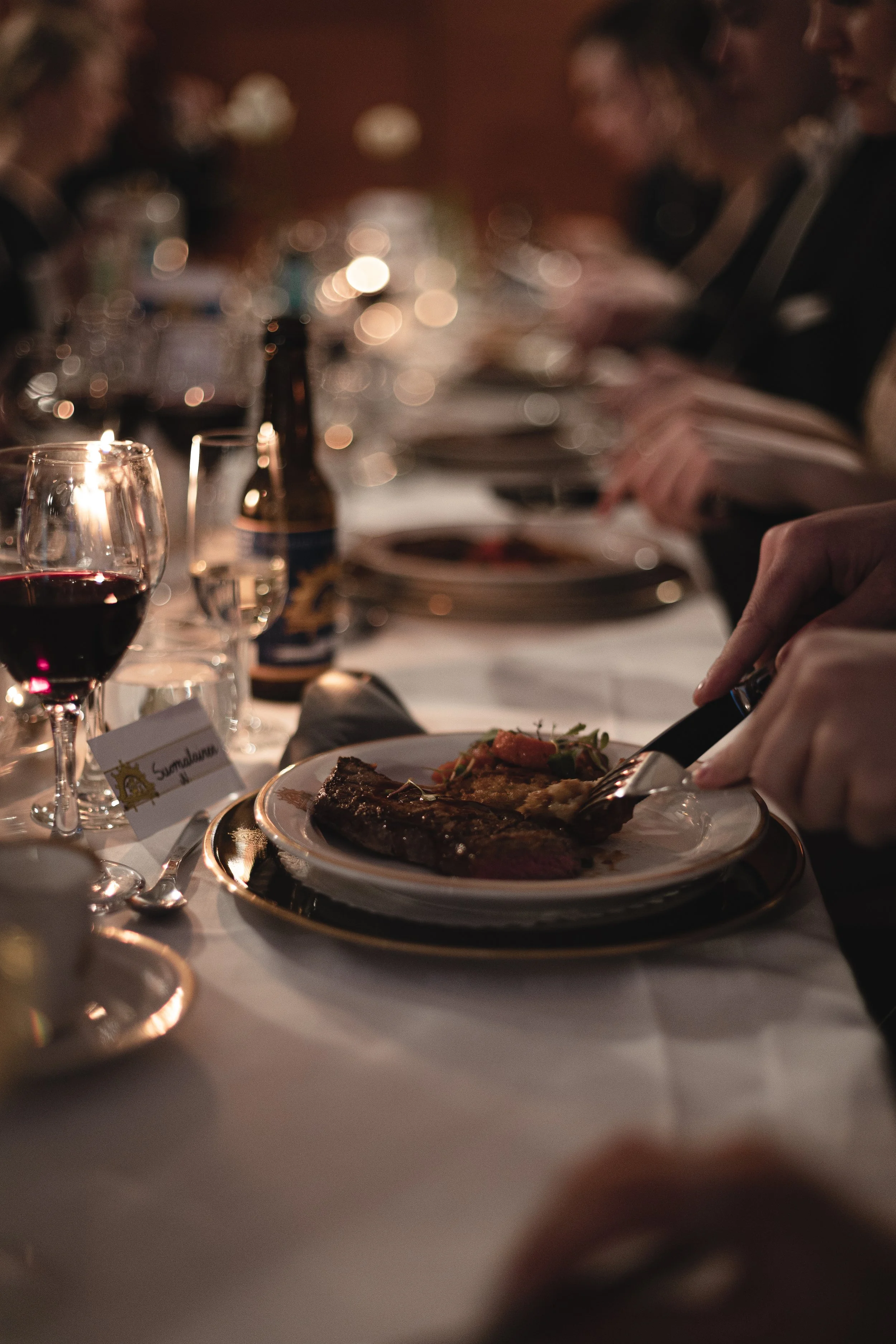 People dining at a formal dinner table with wine glasses and plates of food.