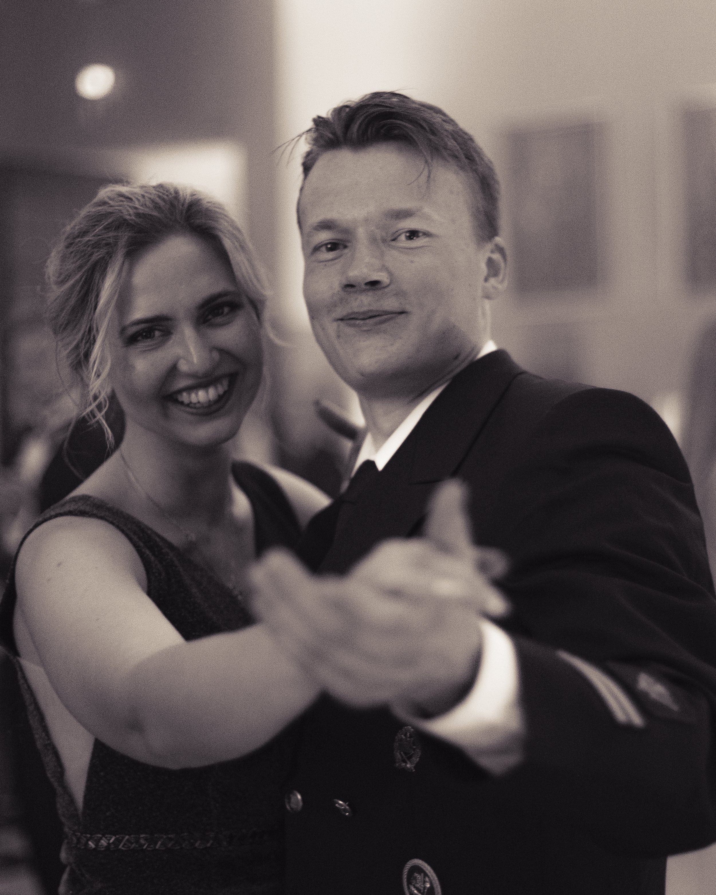 A man and woman dancing together, smiling, in formal attire at an event.