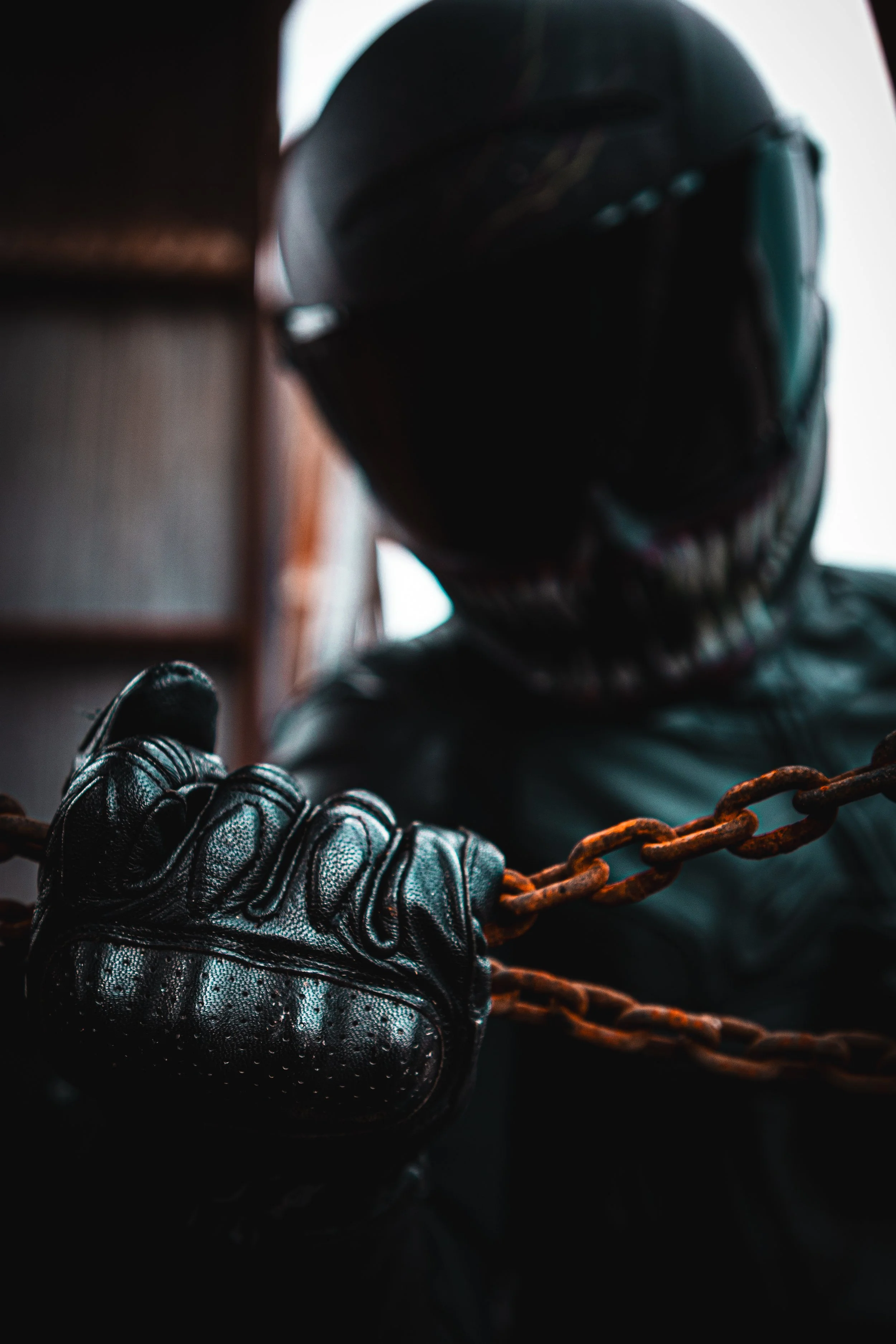 Person wearing a black helmet, leather gloves, and black jacket, holding onto a rusty chain.
