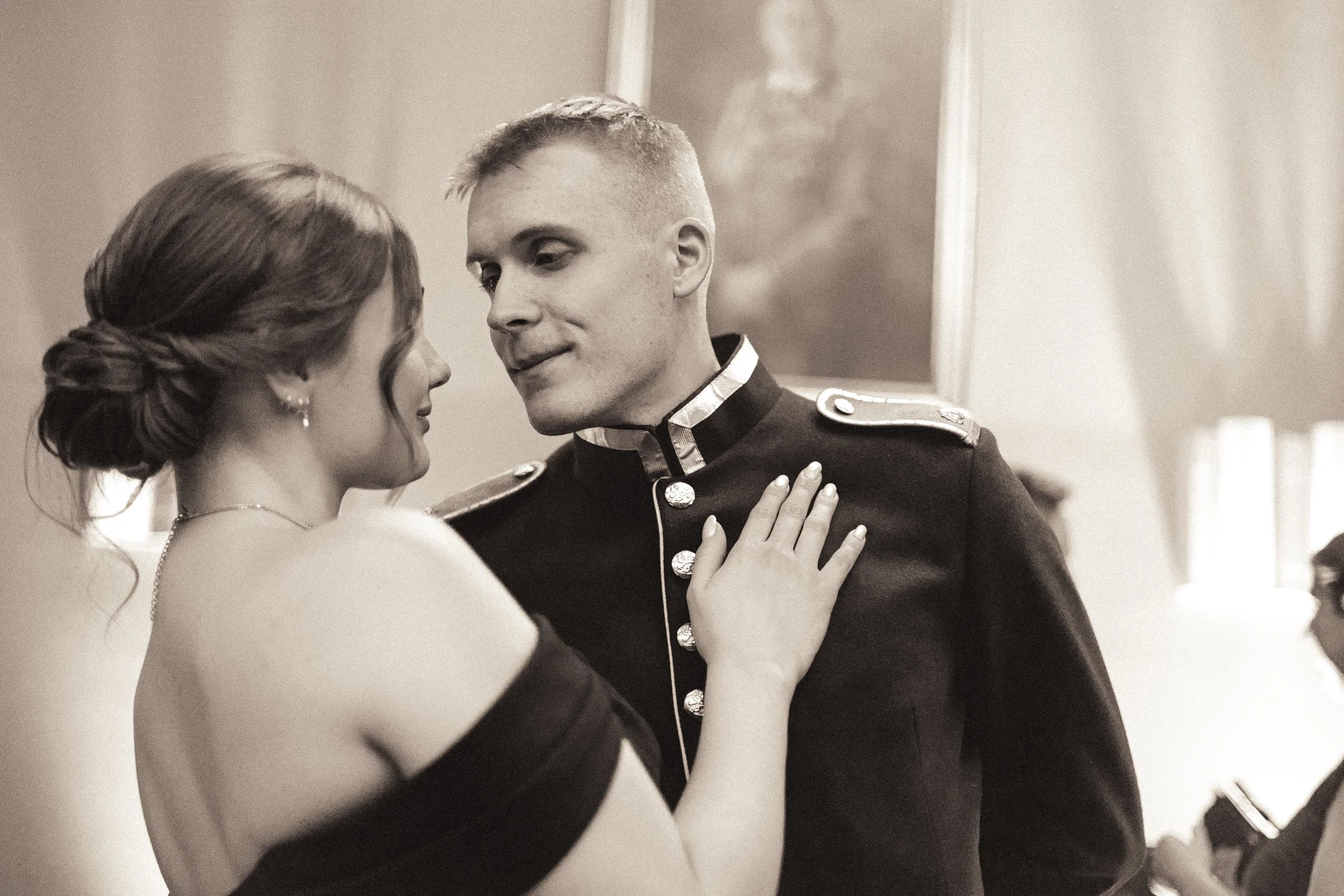 A woman in an elegant dress and a man in a military uniform dance closely, with the woman resting her hand on the man's chest in a formal setting.