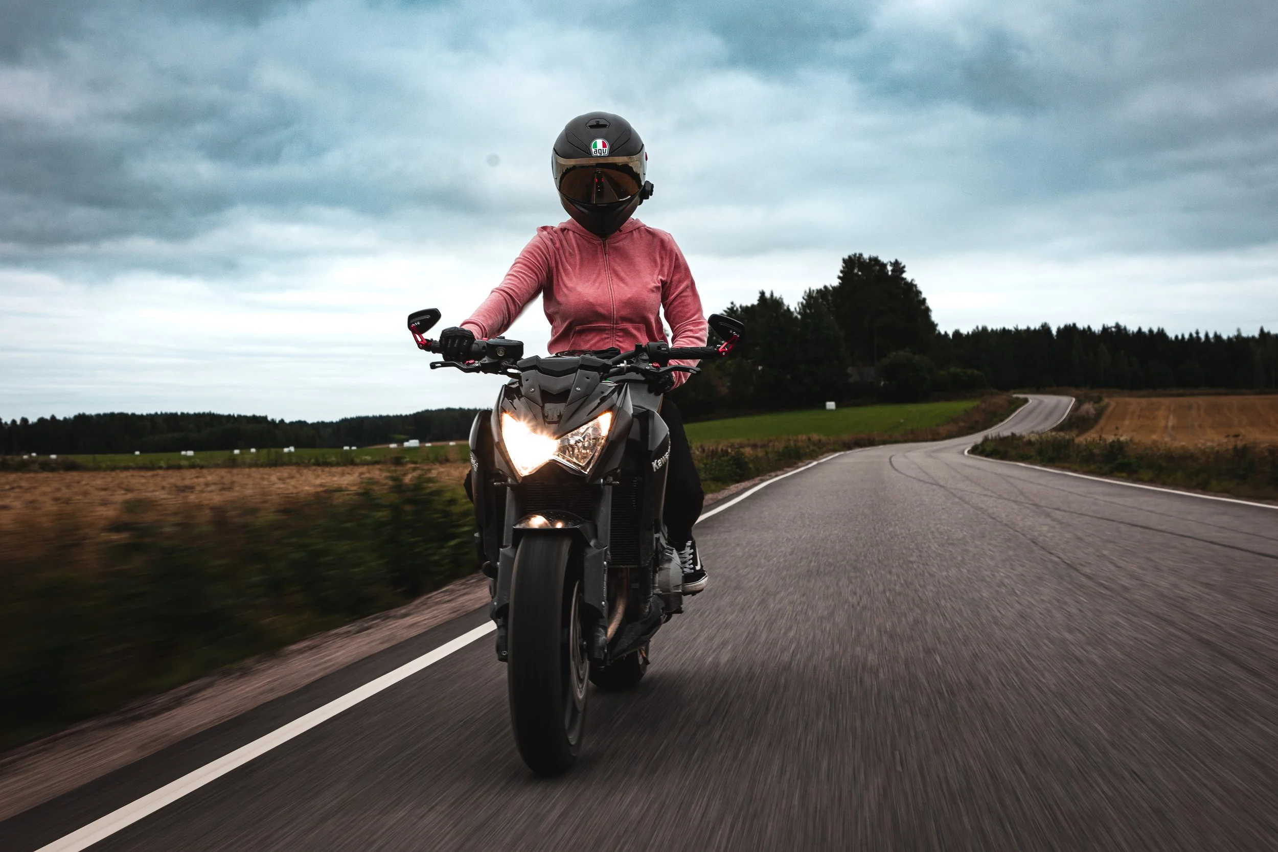Person riding a motorcycle on a rural road with cloudy sky.