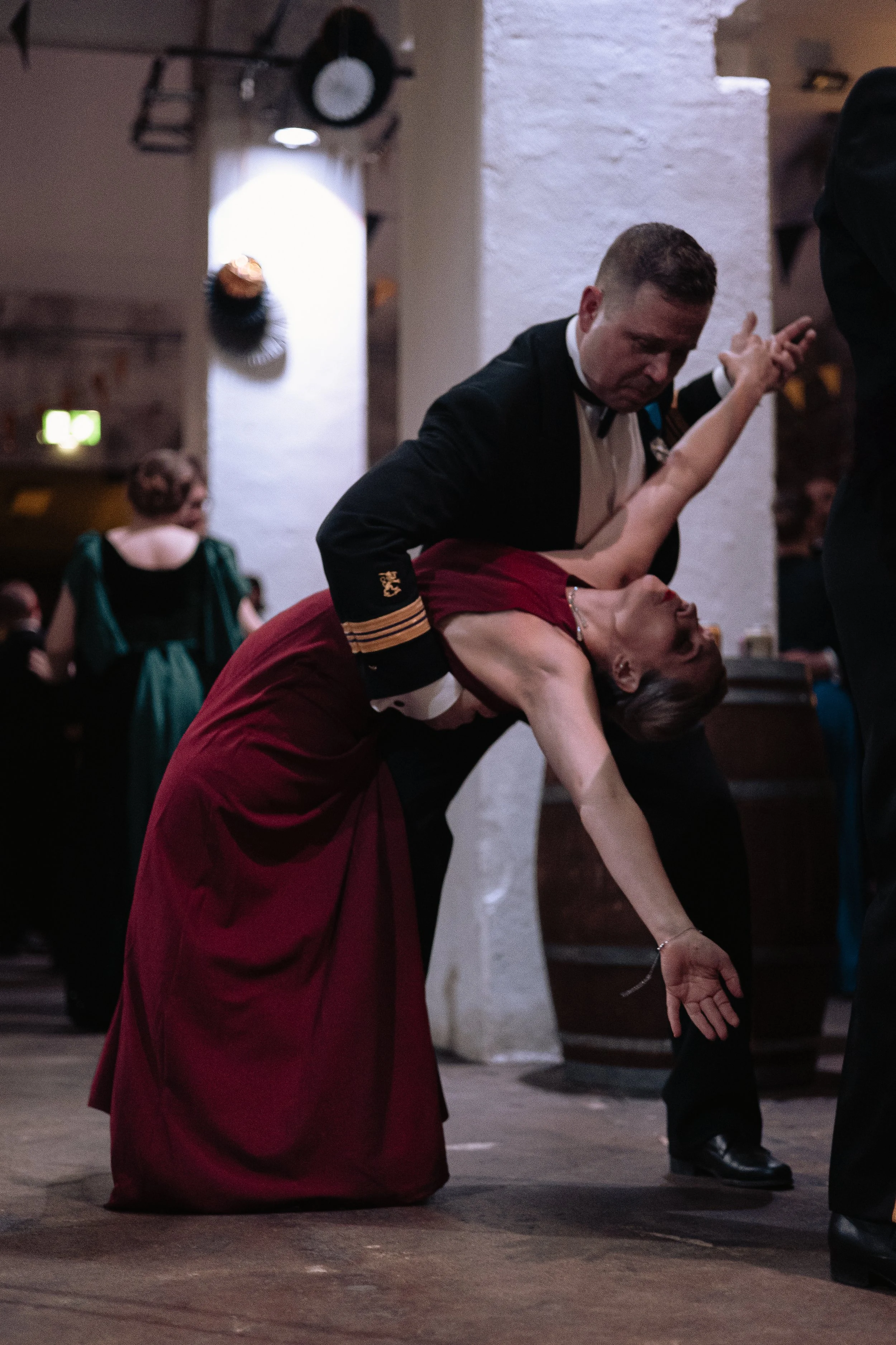 A man and a woman are dancing passionately at a formal event. The woman is leaning back with her arm extended downward, and the man is supporting her with his arm around her waist.