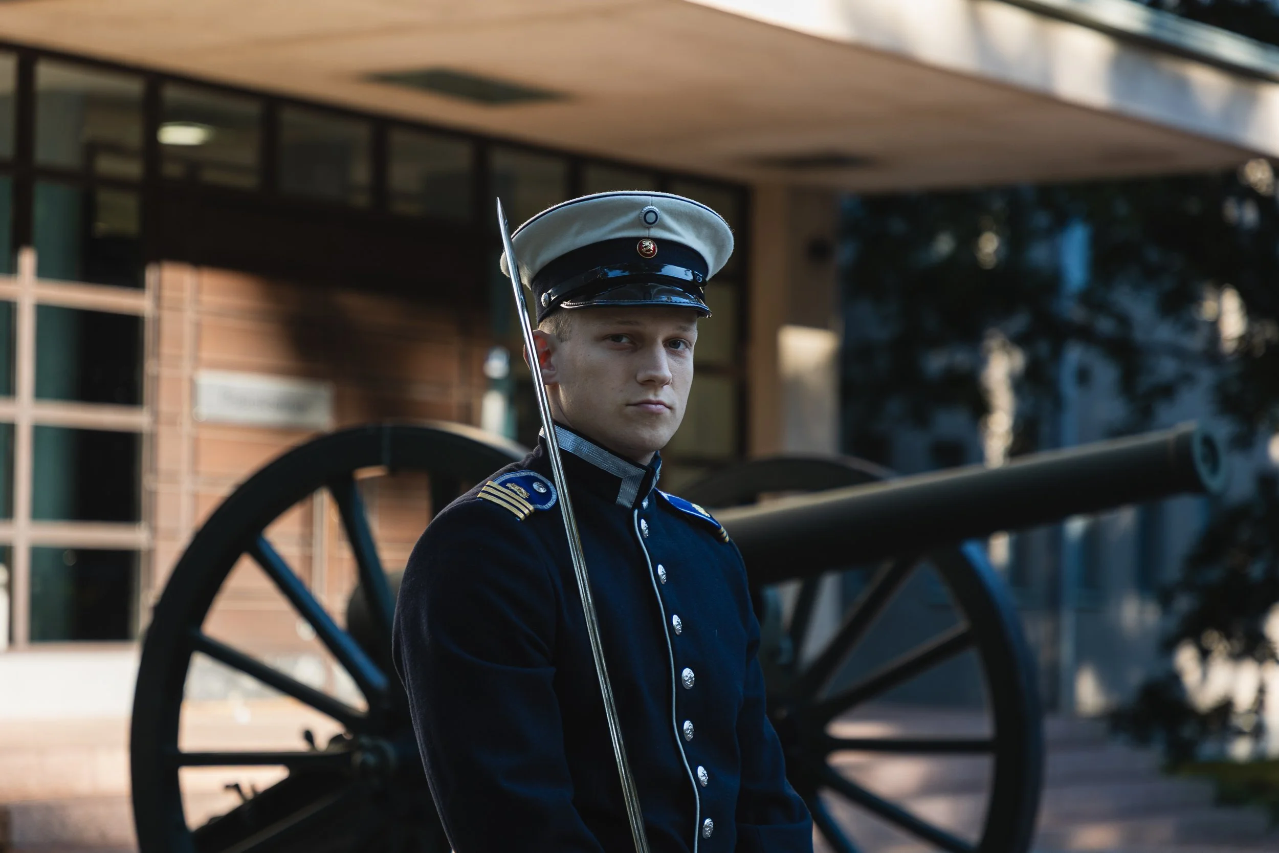 Young man in a historical military uniform standing near battlefield cannon with a building in the background during daytime