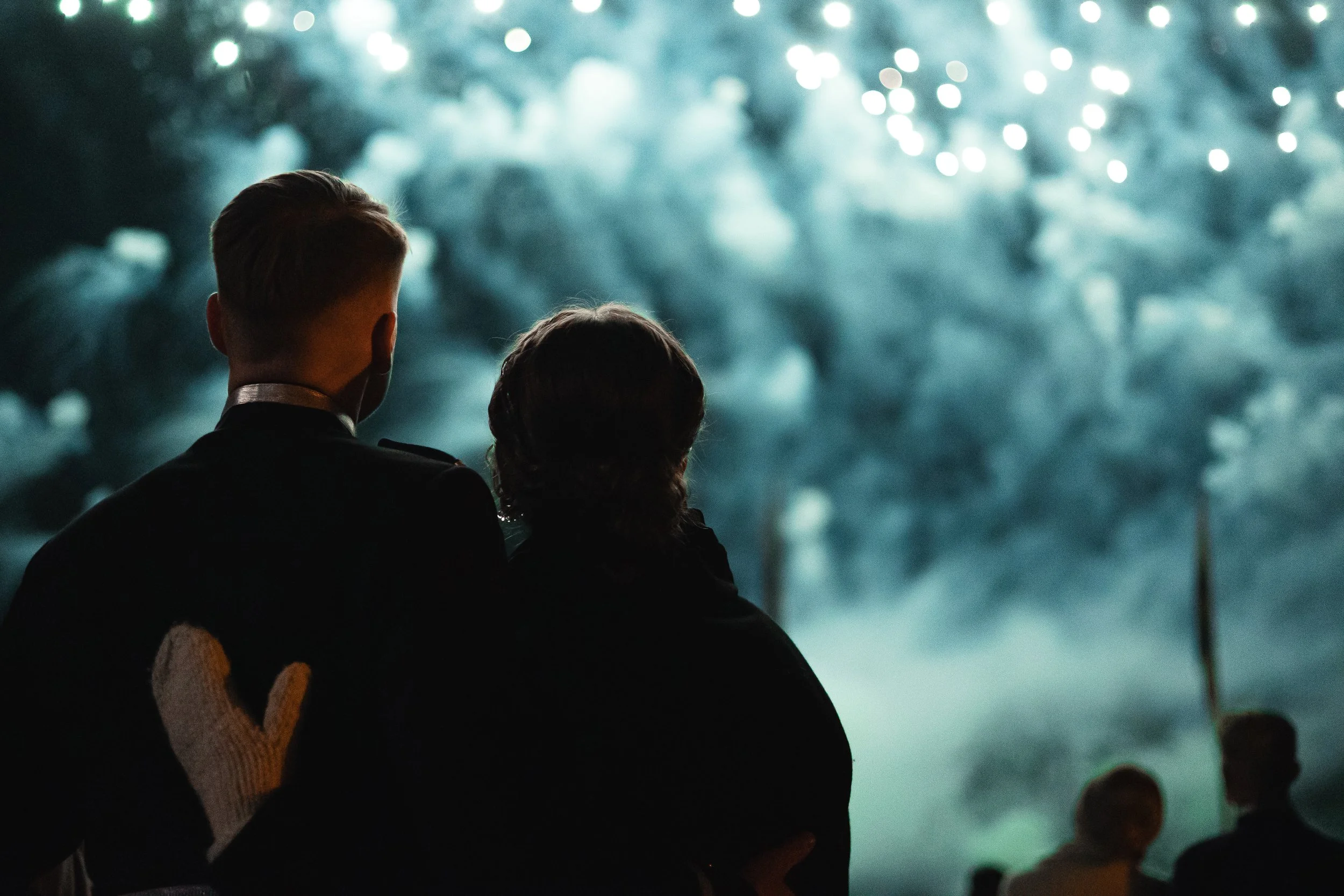 Silhouettes of people watching fireworks at night.