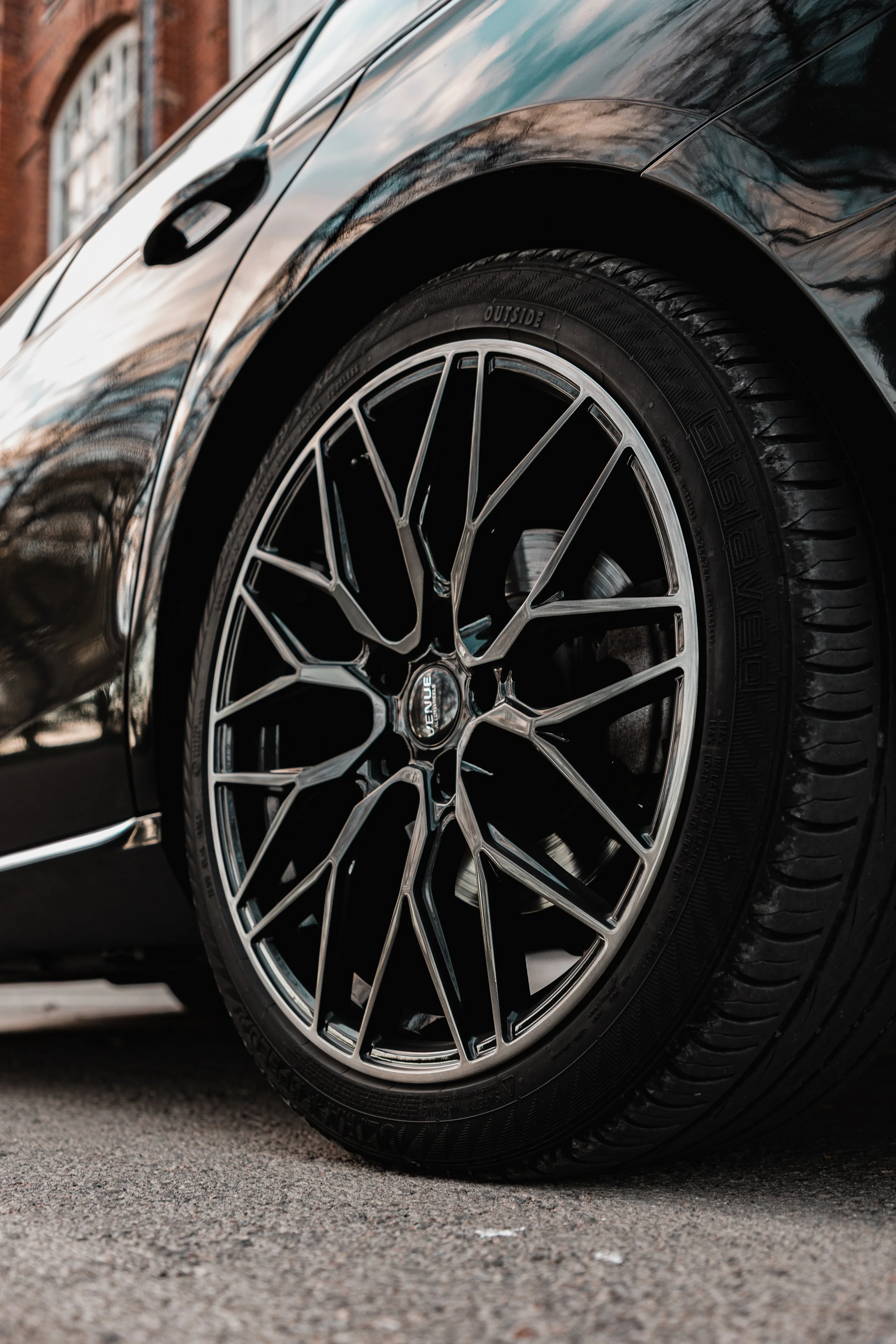 Close-up of a luxury black car with stylish silver alloy wheels parked on a city street.