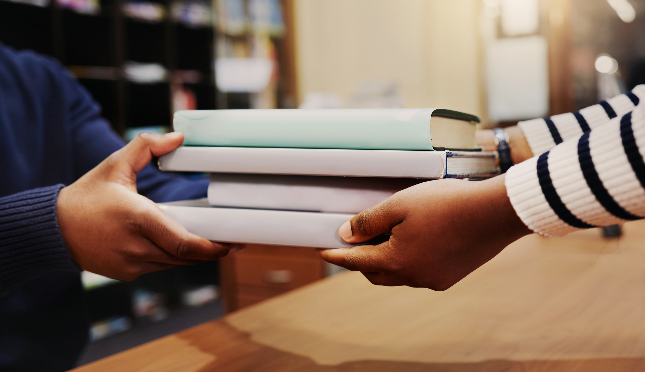 Two people exchanging a stack of books in a library or classroom.
