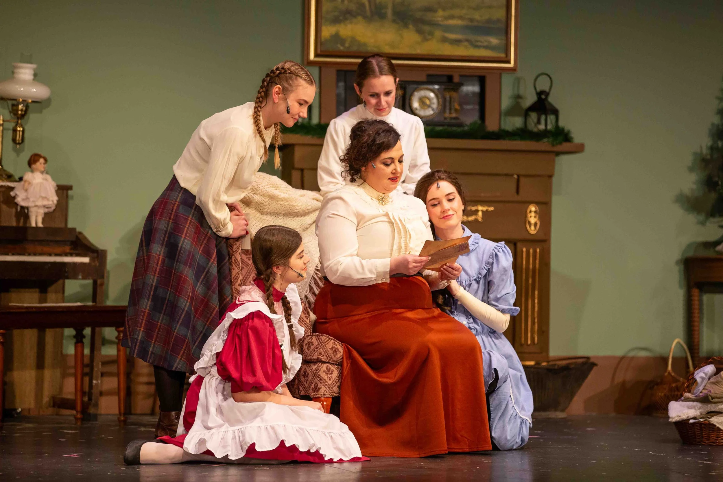 A woman surrounded by 4 girls sitting on stage at The Strand Theater performing Little Women.