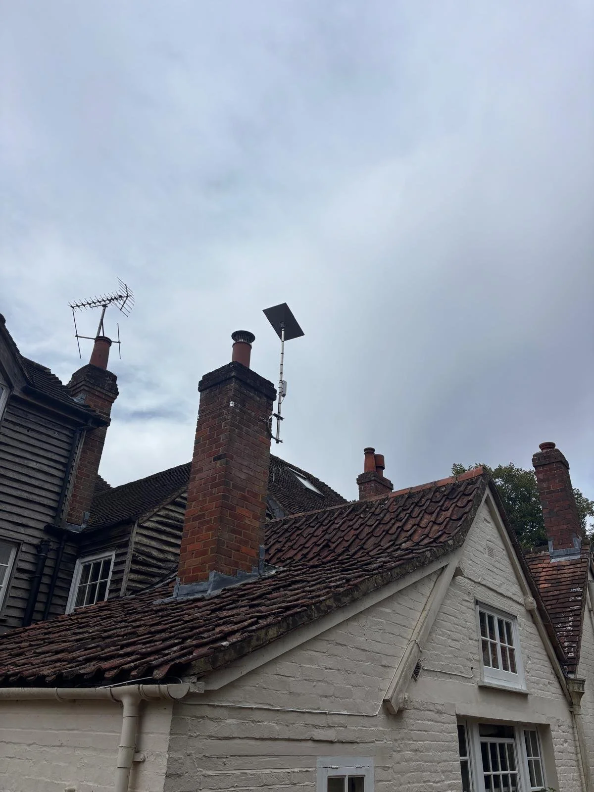 Rooftops of old brick houses with Starlink installed on the chimney against a cloudy sky 