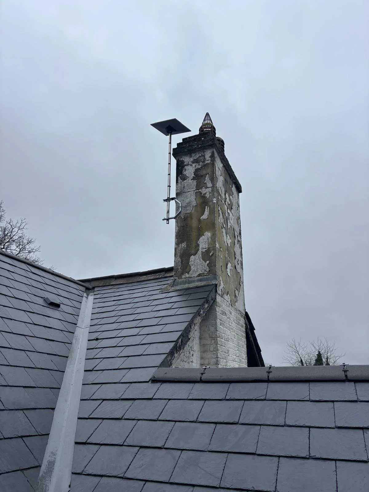 View of a chimney with Starlink internet mounted on the side, against a cloudy day.