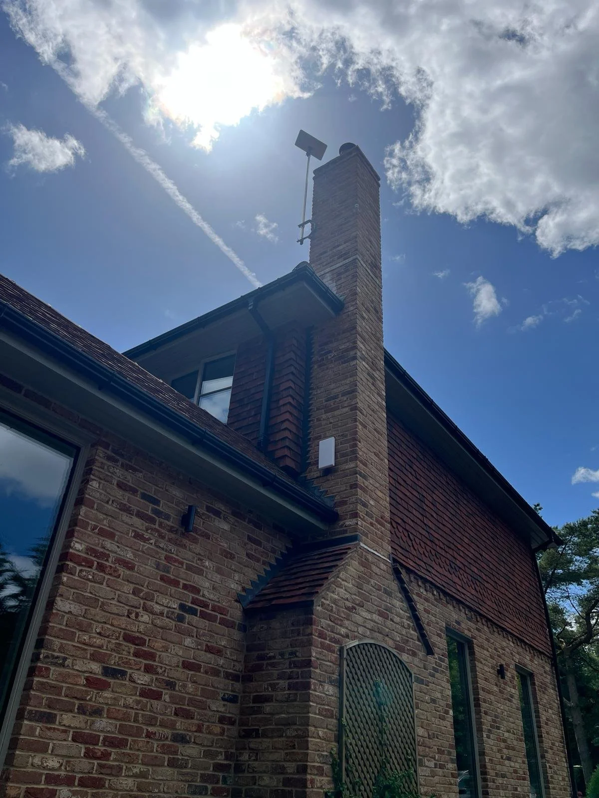 Back corner of a brick house with Starlink internet installed on the side of the chimney