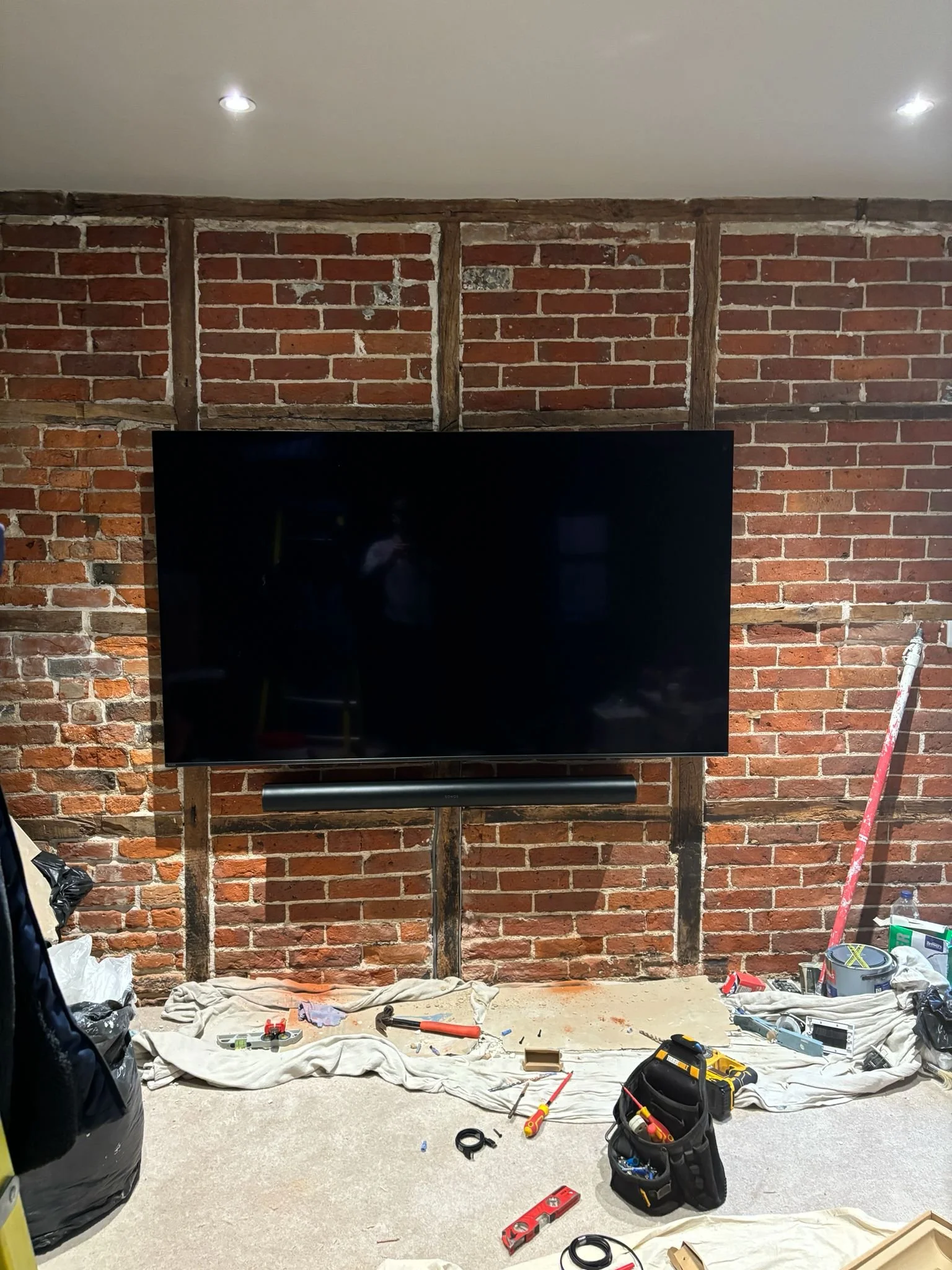 A large flat-screen TV mounted on a brick and wood wall, with tools and supplies scattered on the floor below during a home renovation.