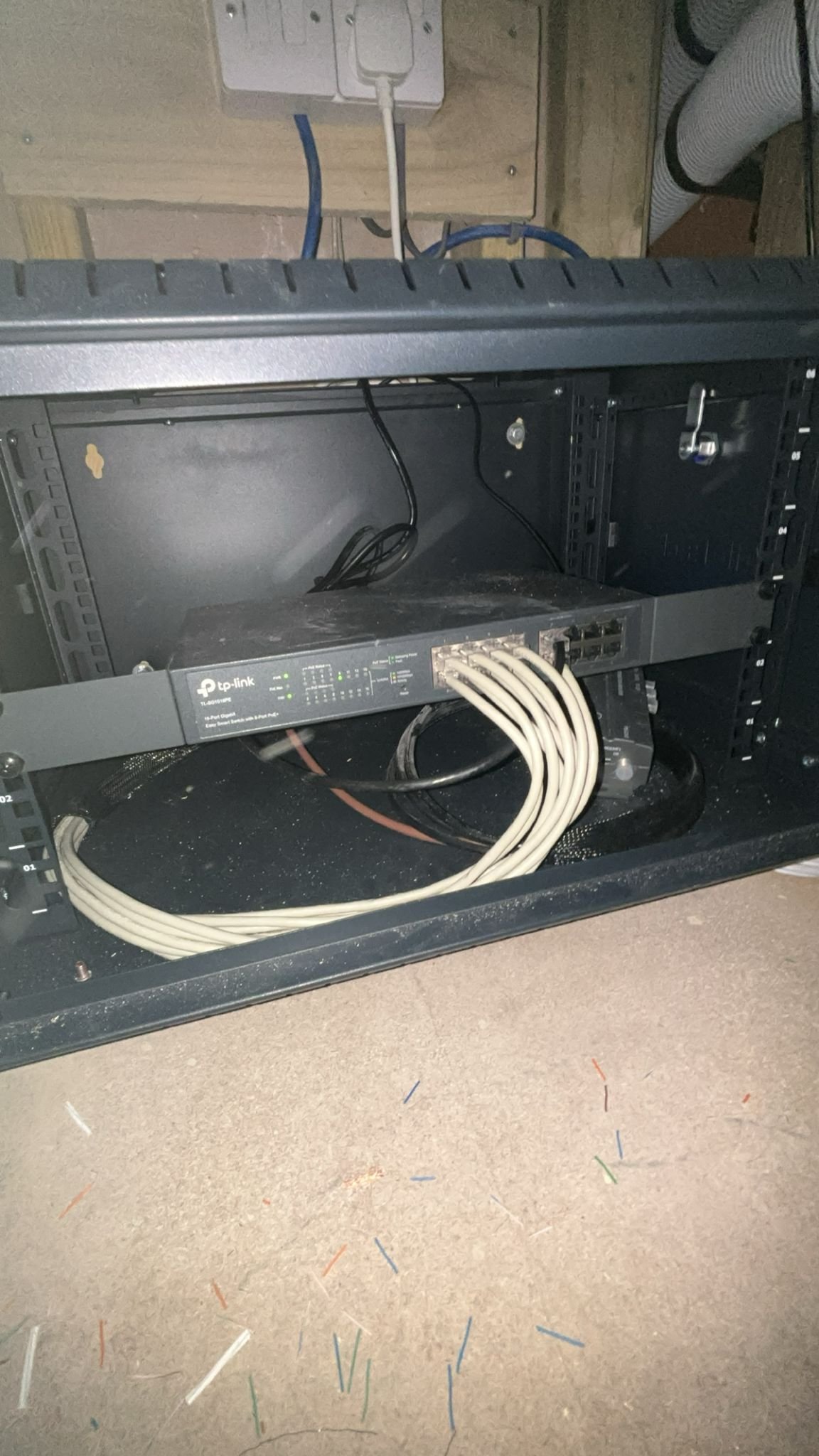 Inside a server rack, an Ethernet switch with multiple ports and green indicator lights, connected with white and black cables, is mounted at the bottom of the rack.