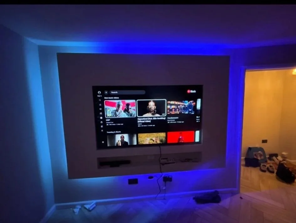 Living room with a TV displaying a video streaming app, illuminated by blue LED lights, with a darkened wall.