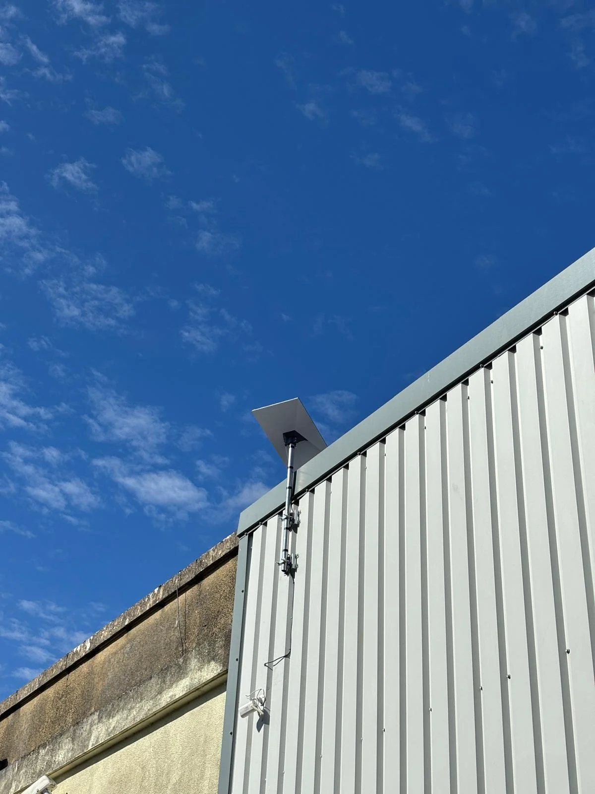 Close-up of a building with a metal exterior and a Starlink installed on the corner, under a blue sky with a few clouds.