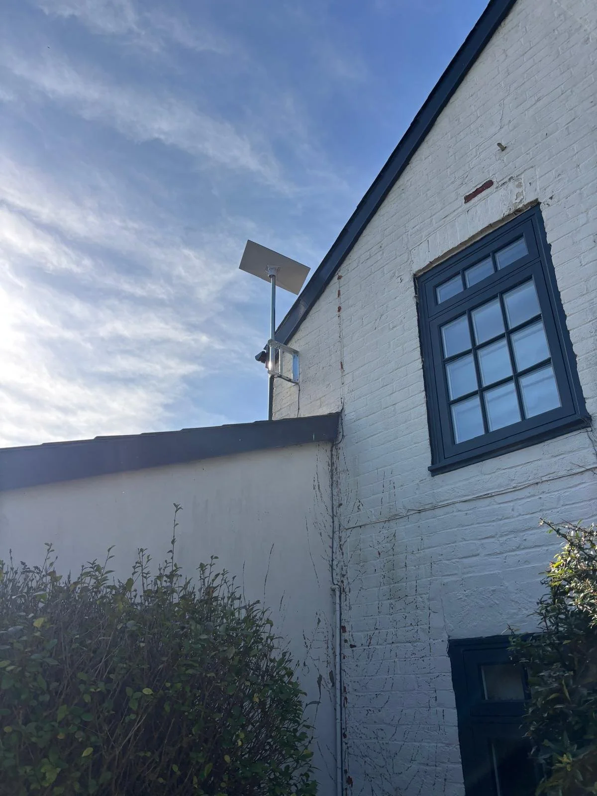 Exterior side of a white brick house with black window frames, a small window near the lower right, a blue sky with some clouds, and a Starlink dish mounted on the side of the house.