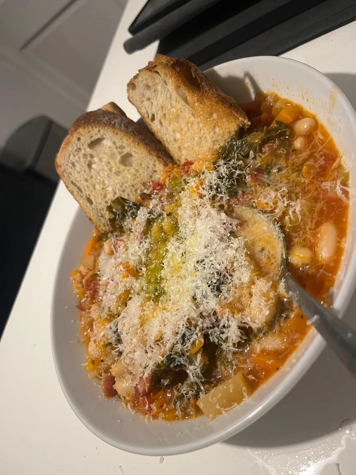 A bowl of vegetable soup topped with shredded cheese and served with two slices of bread.