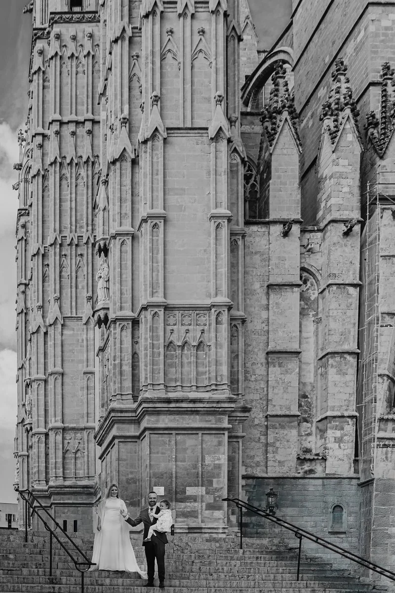 Una pareja con un niño pequeño en las escaleras de una catedral gótica, probablemente después de una boda.