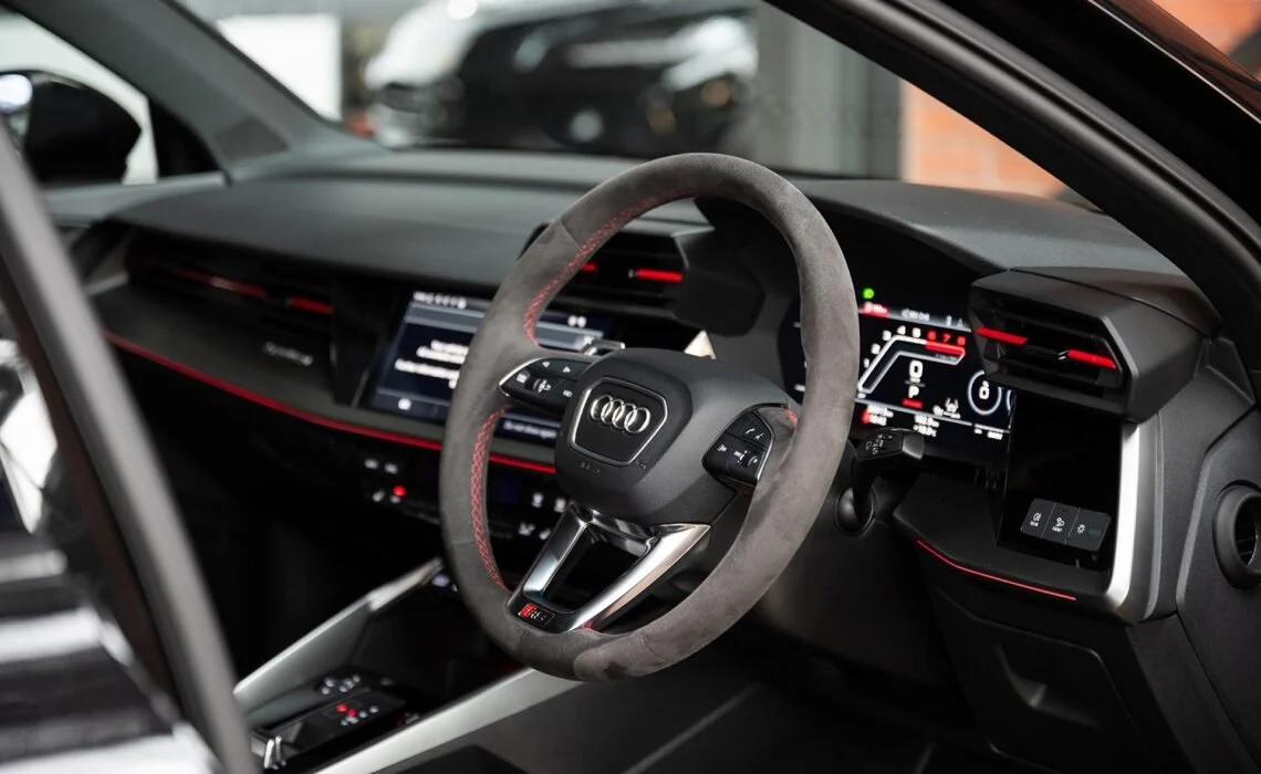 Interior of an Audi vehicle featuring a steering wheel with Audi logo, digital dashboard, and modern dashboard controls.