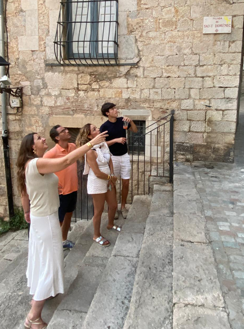 Four people standing on stone steps outside a stone building, taking a photo of a nearby window.