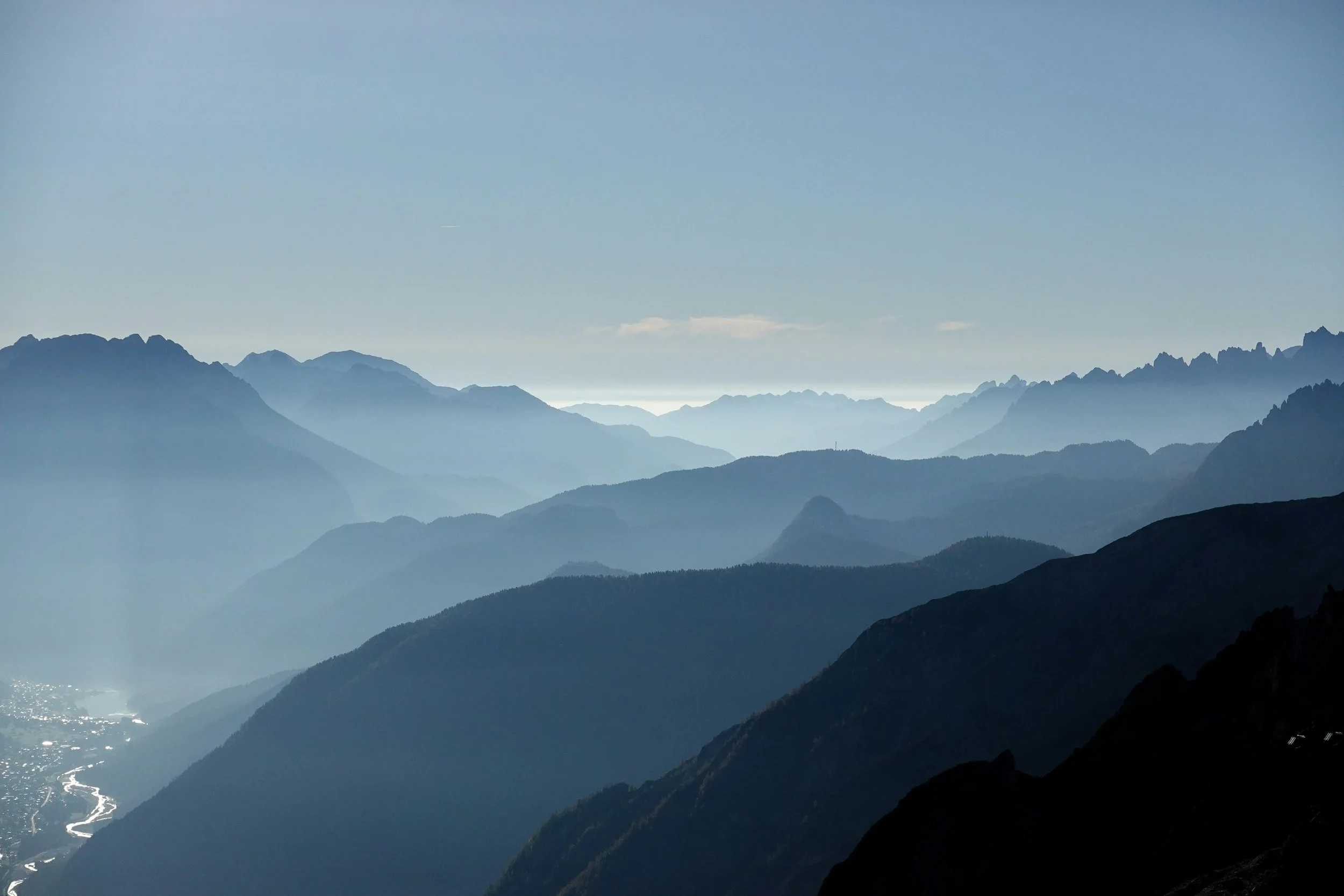 Layers of blue misty mountains under a clear sky, with a river visible in the valley on the left.