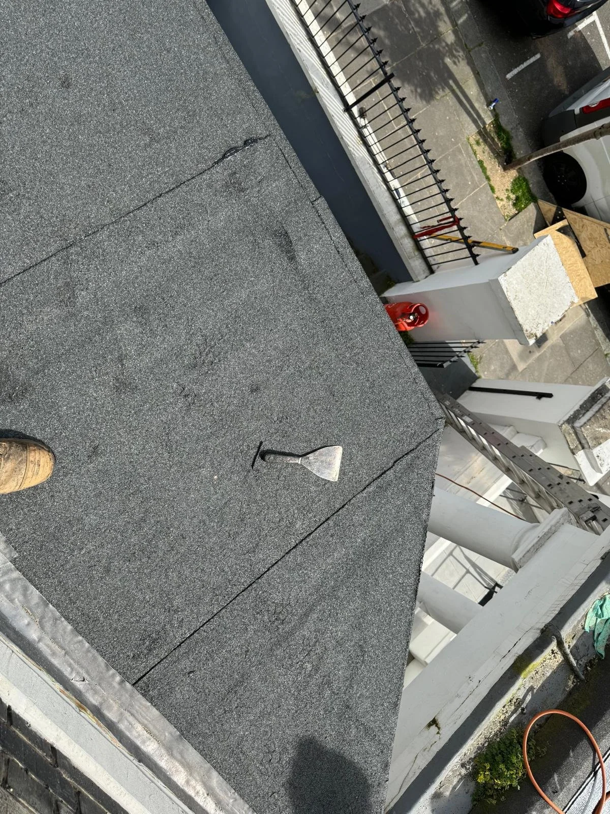 View of a flat roof with a single shovel lying on it, surrounded by various construction and building elements in an urban area.