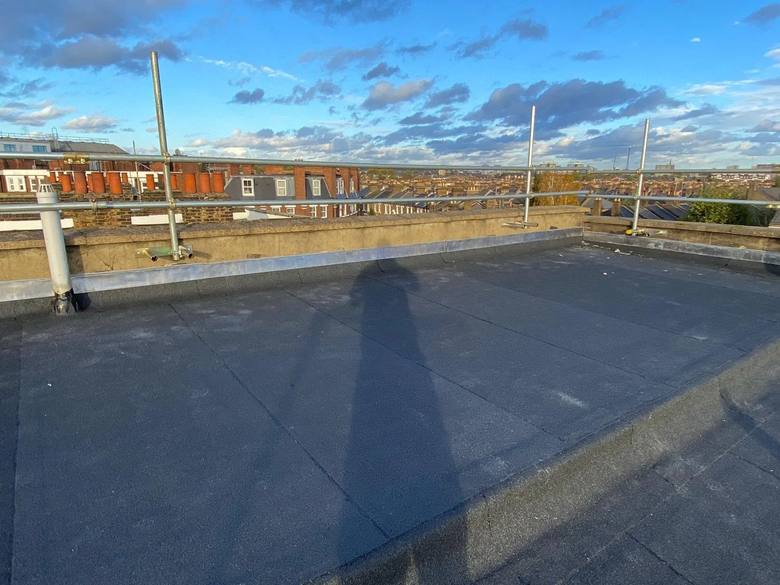 View of a rooftop with safety railings, overlooking neighboring rooftops and a partly cloudy sky at sunset.